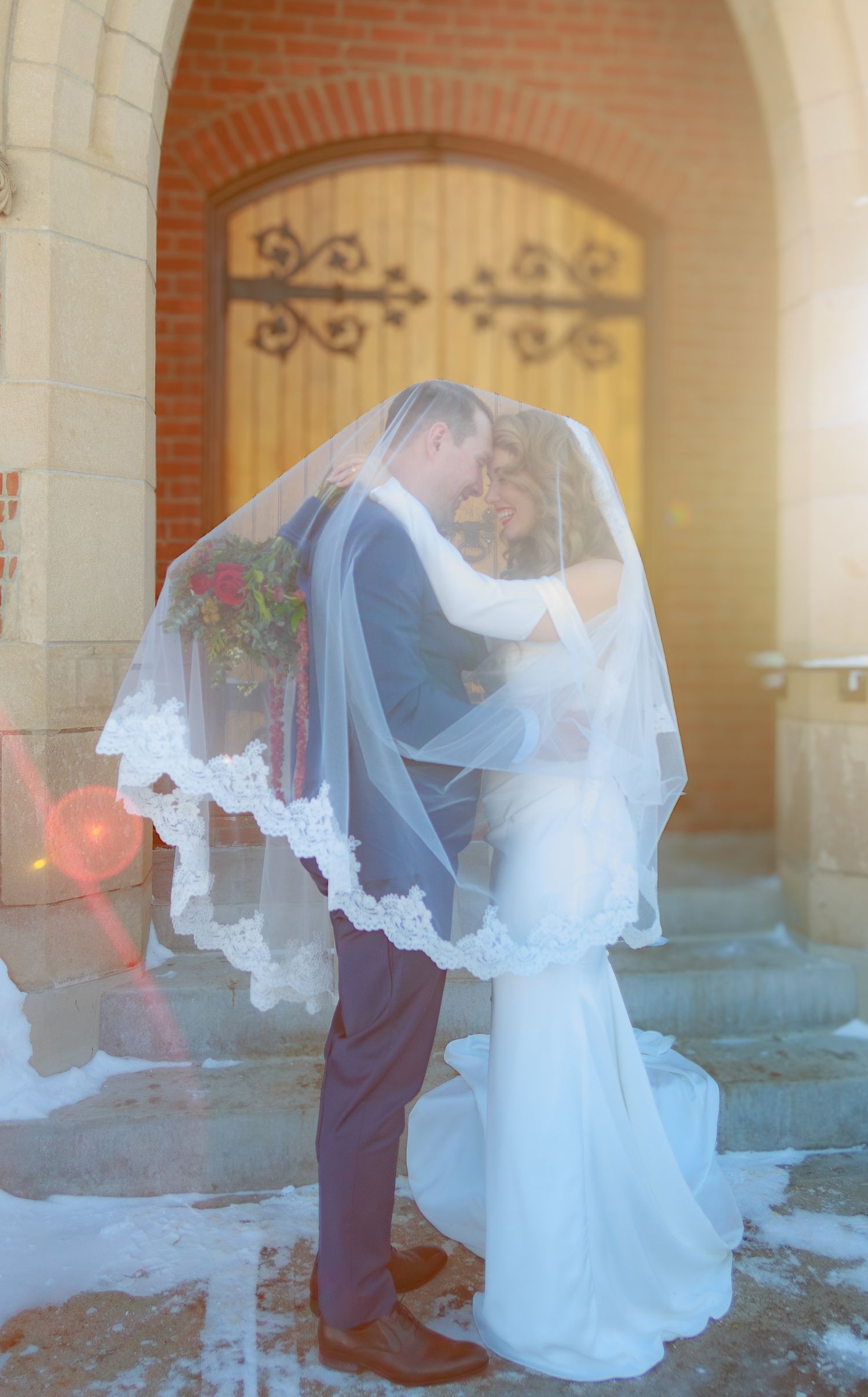 Sunlit wedding portrait with flowing veil against classic brick archway backdrop.