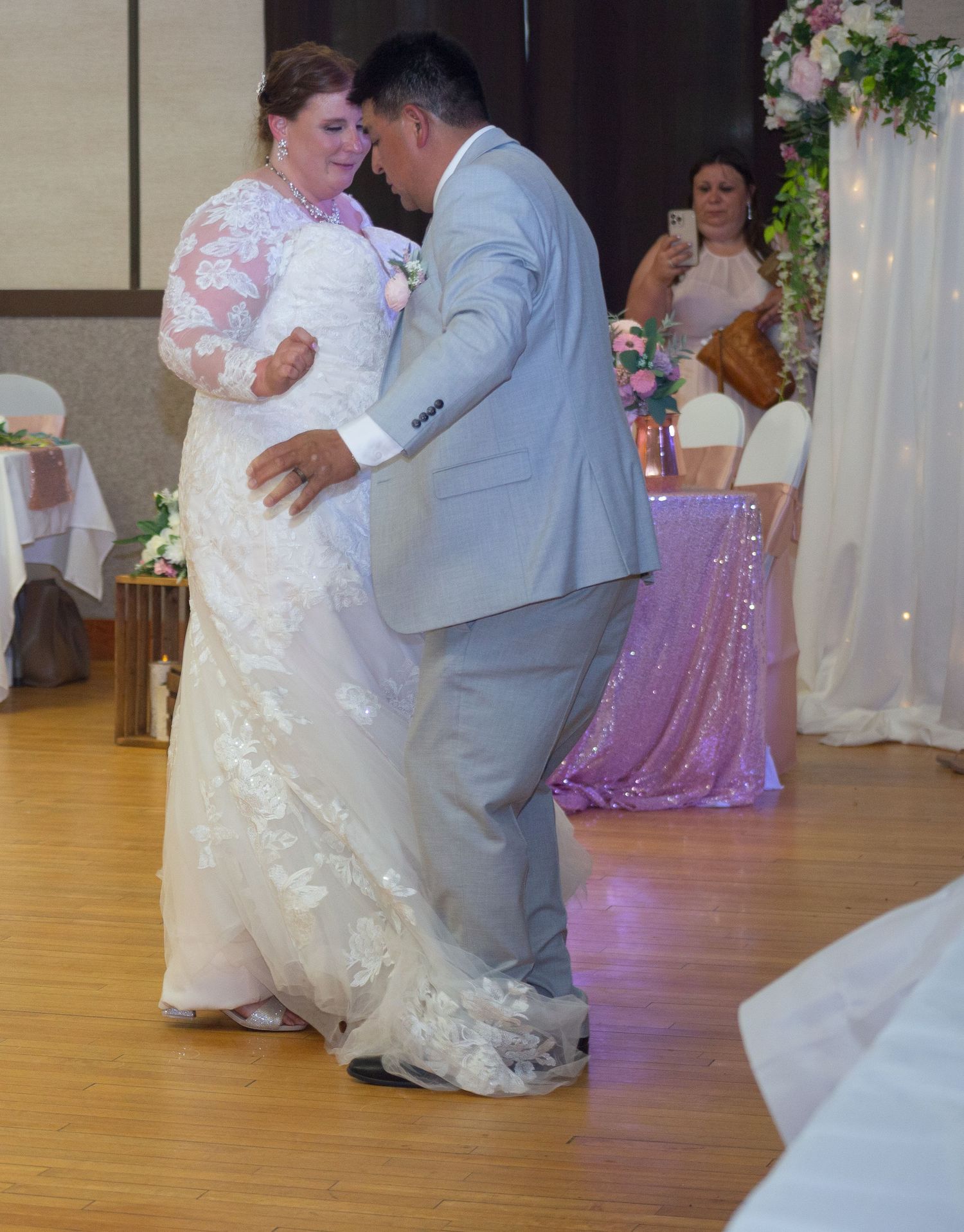 Couple shares their first dance on wooden floor during wedding reception.