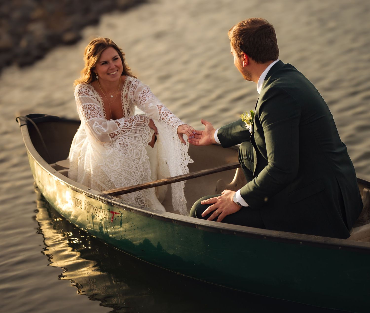 A bride and groom paddle together in a green canoe during their lakeside wedding photoshoot.