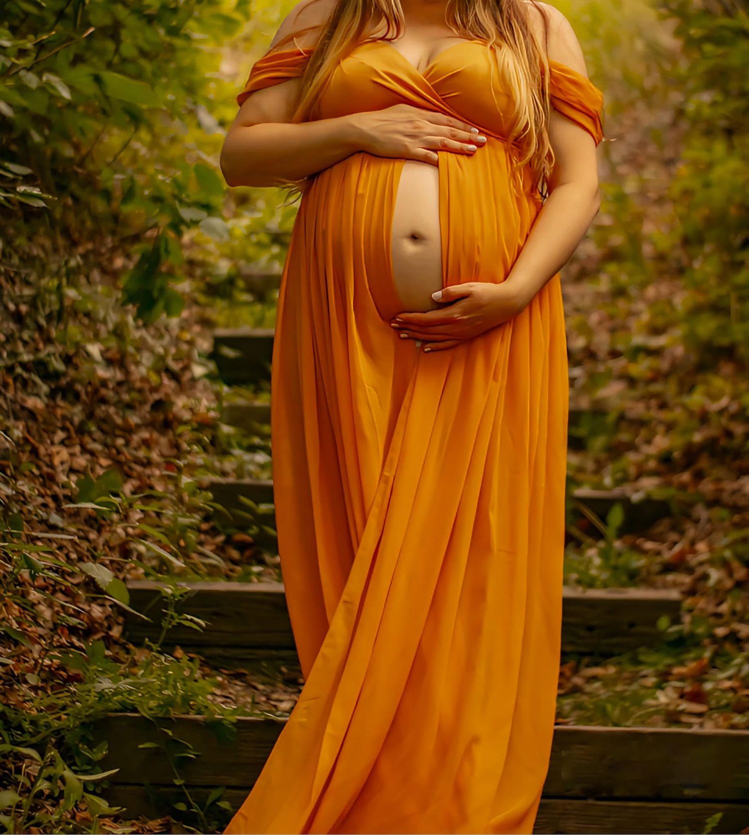An orange off-shoulder maternity dress frames a tender moment on wooden steps in nature.