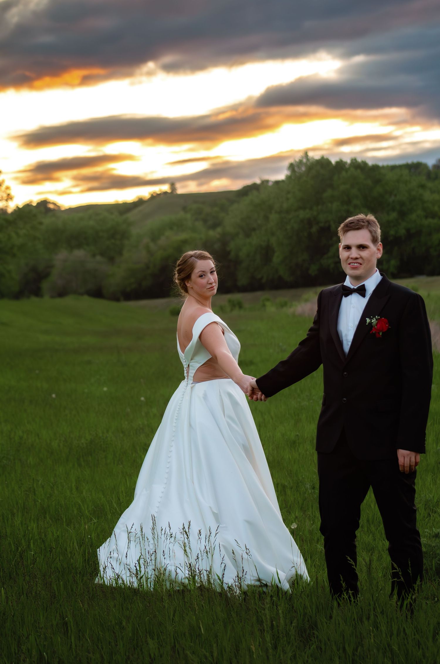 A wedding couple poses in a grassy field at sunset.