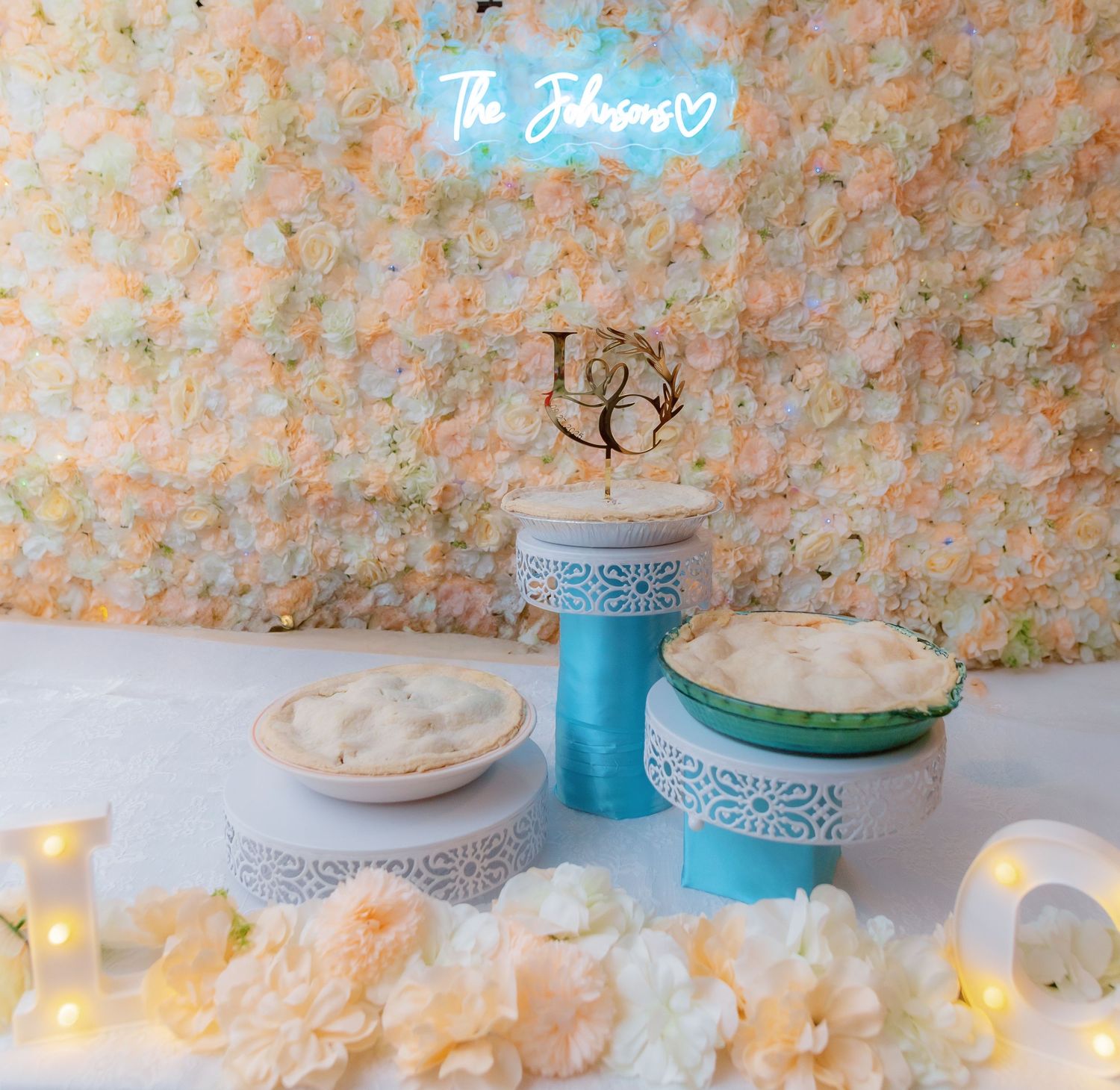 Wedding dessert table with blue accents and neon sign featuring white cakes and romantic lighting.