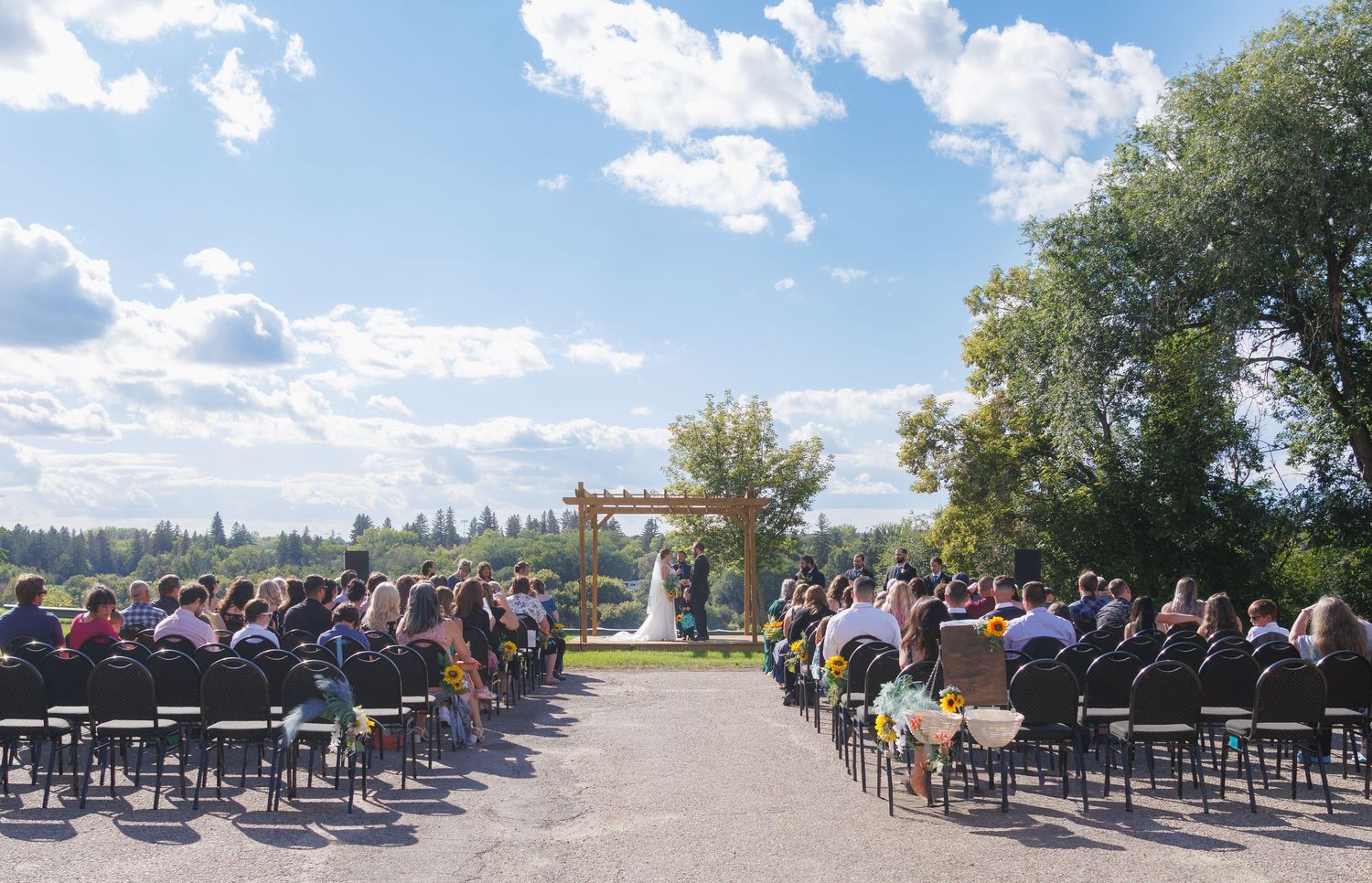 Outdoor wedding ceremony setup with white chairs under blue sky and clouds.