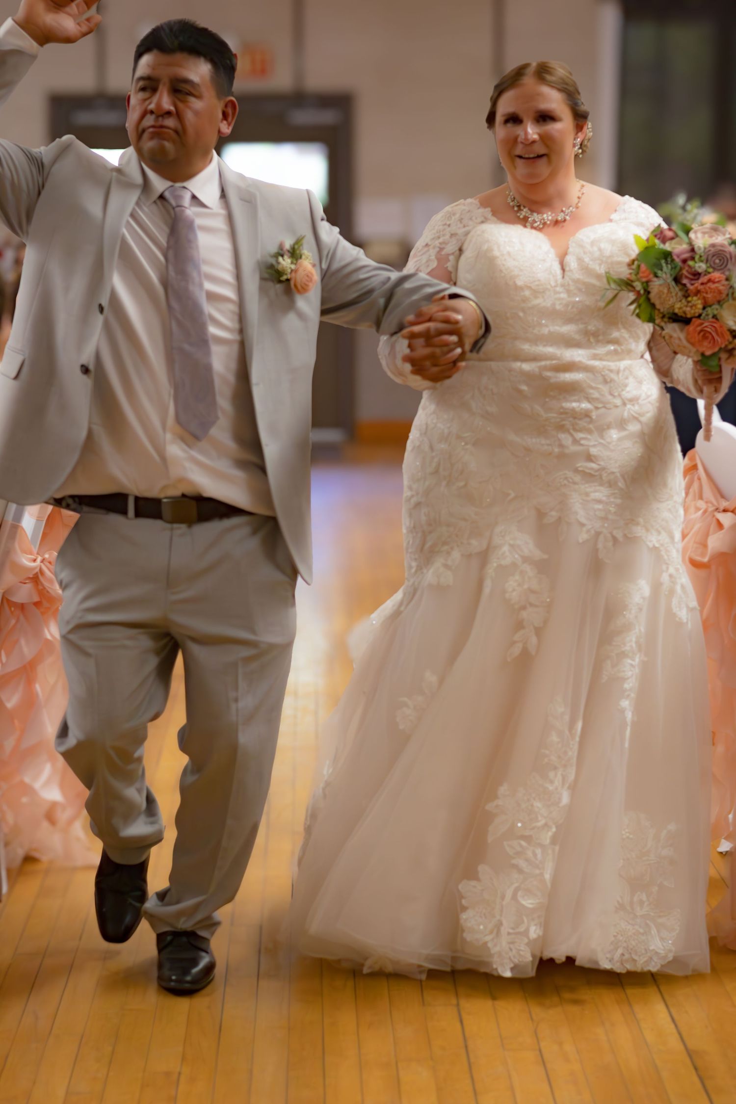 Wedding couple dances energetically on wooden floor during reception celebration.