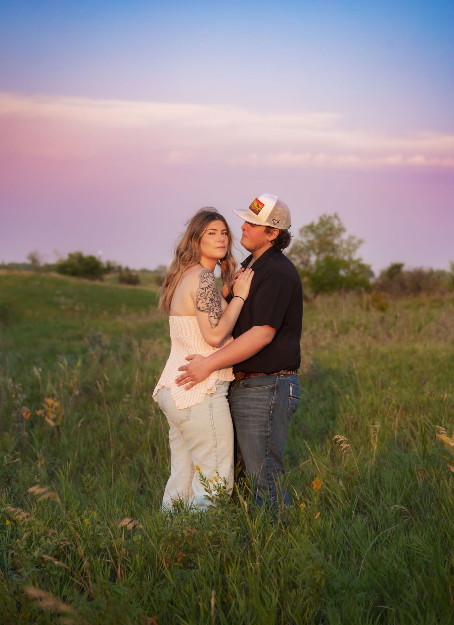 Couple shares intimate moments in a grassy field at sunset.