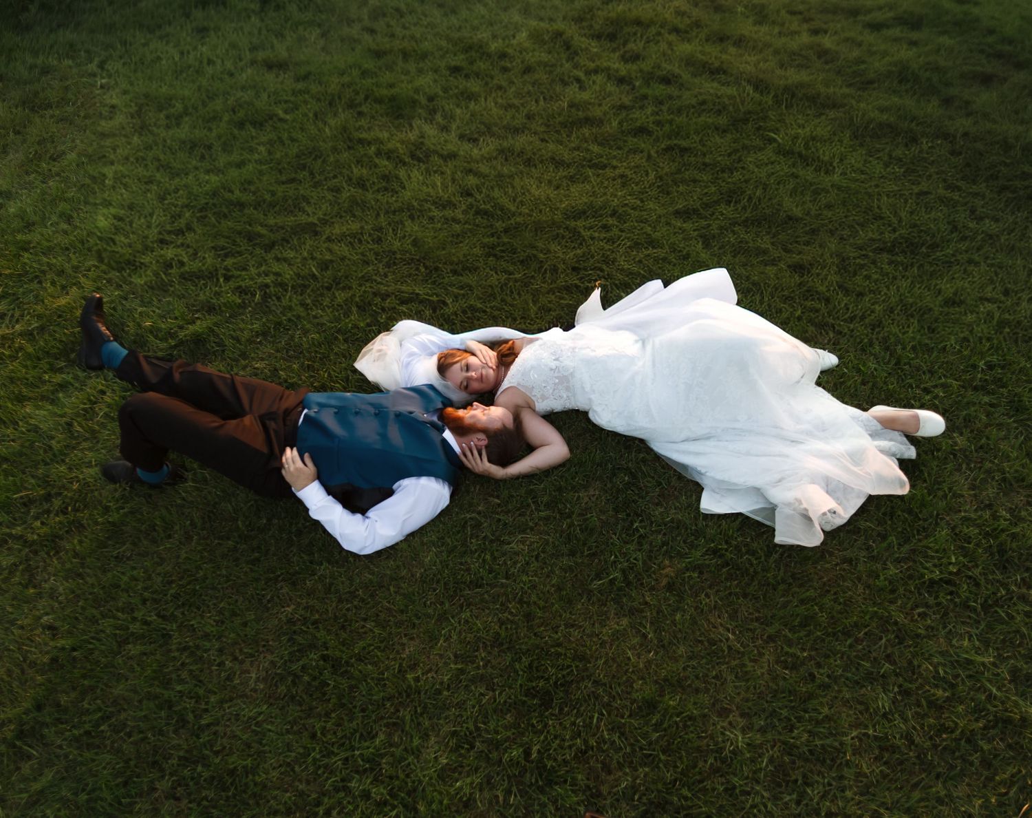 Wedding couple lying on lush green grass during a romantic photoshoot.