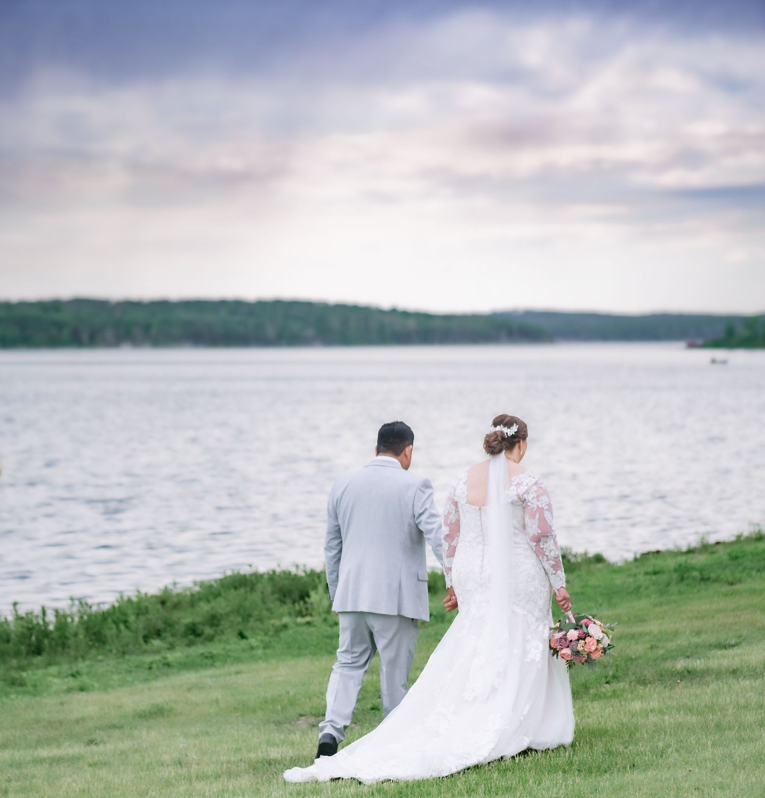 A couple shares a tender moment on grassy shores overlooking a peaceful lake.