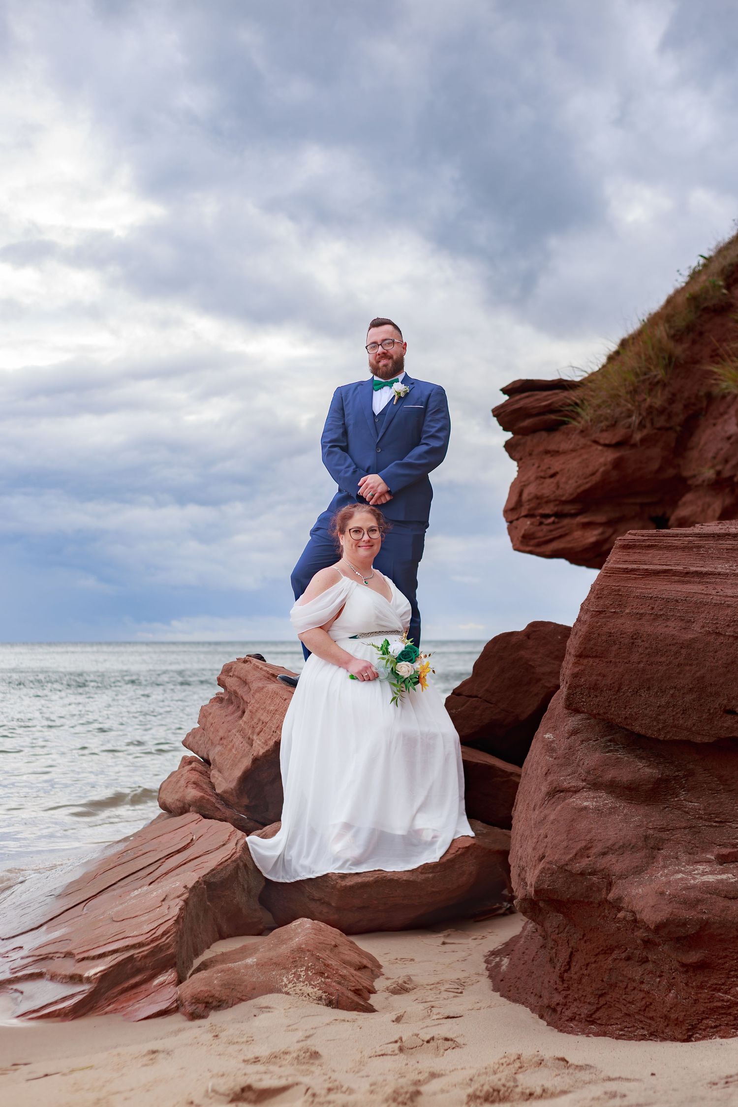 Wedding couple poses on dramatic red rock formations by the ocean.