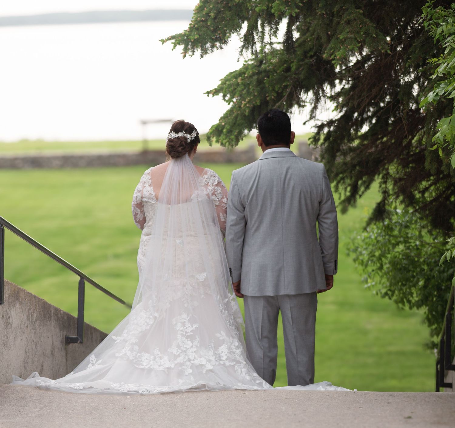 Wedding couple stands together overlooking scenic green landscape from stone terrace.