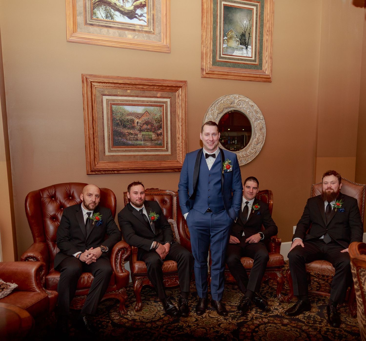 Wedding party members seated in formal attire on leather chairs in an ornate room.