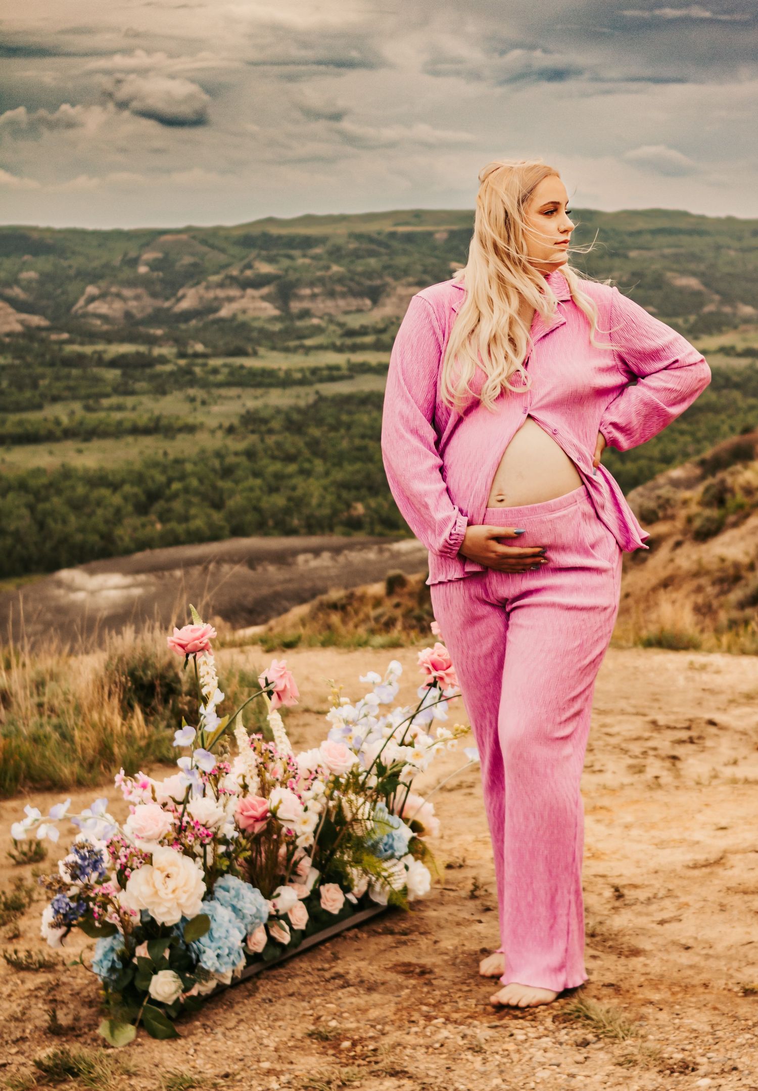 Pink-clad figure posing near elegant floral arrangements on a hilltop overlook.