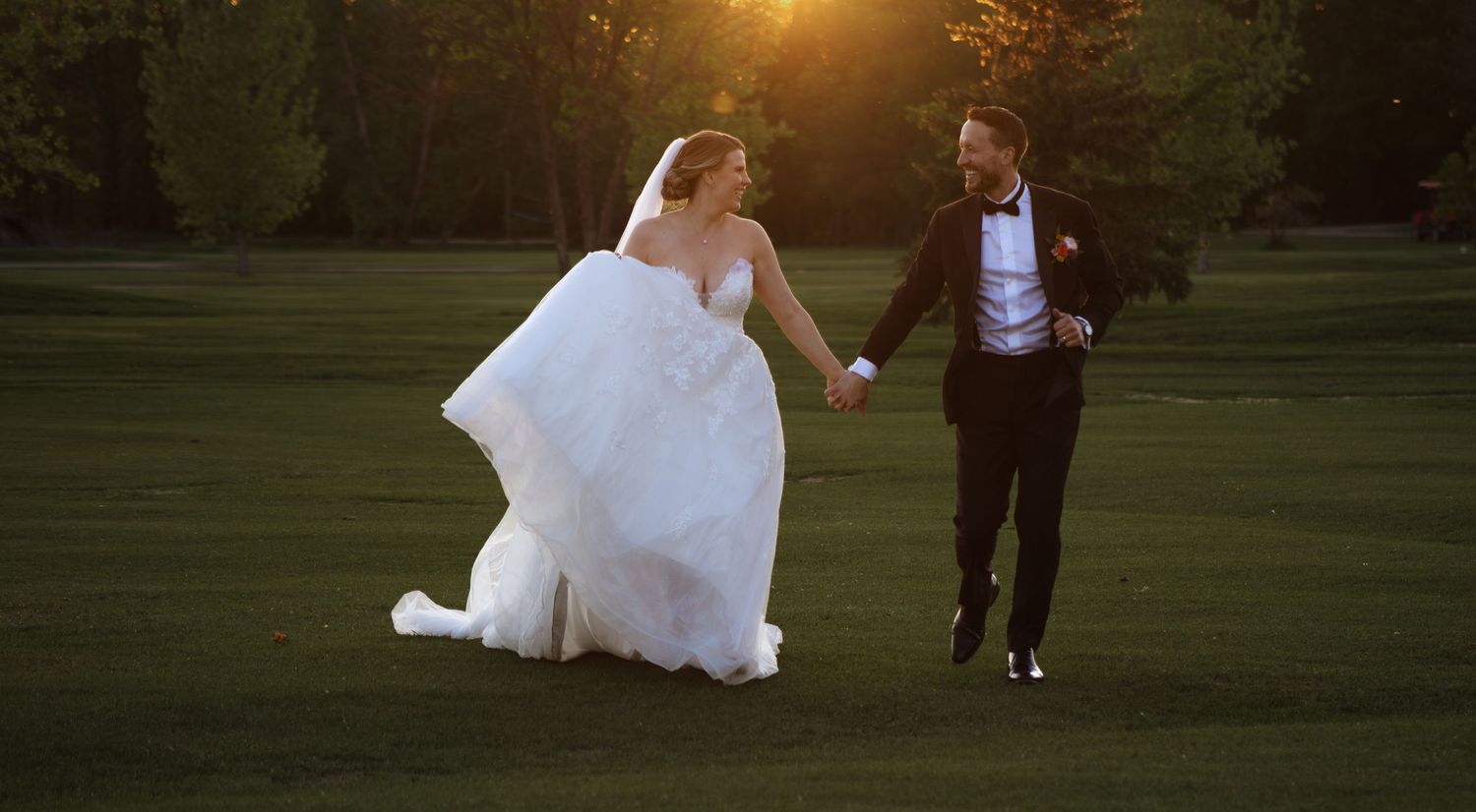 Wedding couple strolling through a park backlit by golden sunset light.