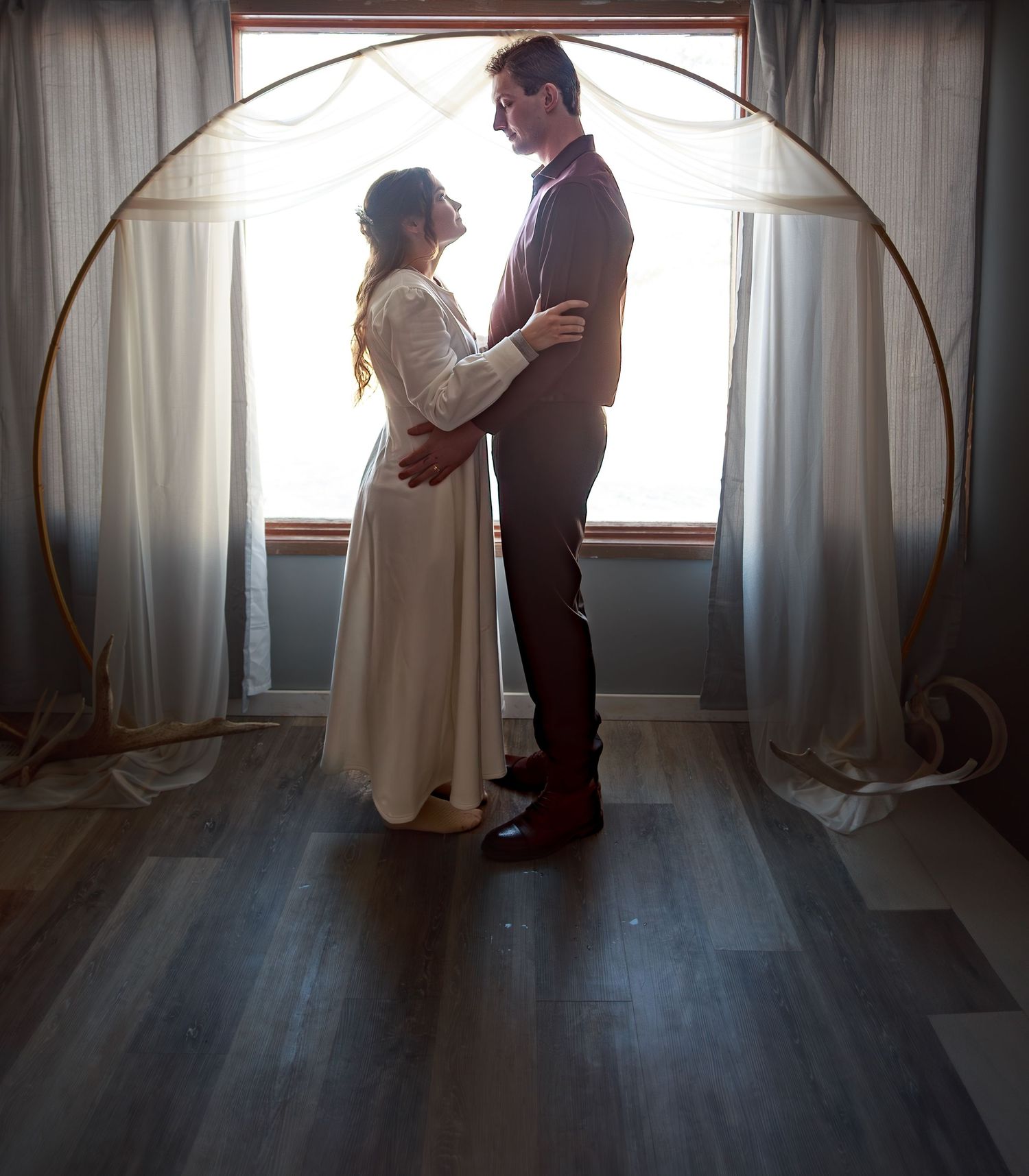 A couple shares an intimate moment in a sunlit room with sheer curtains.