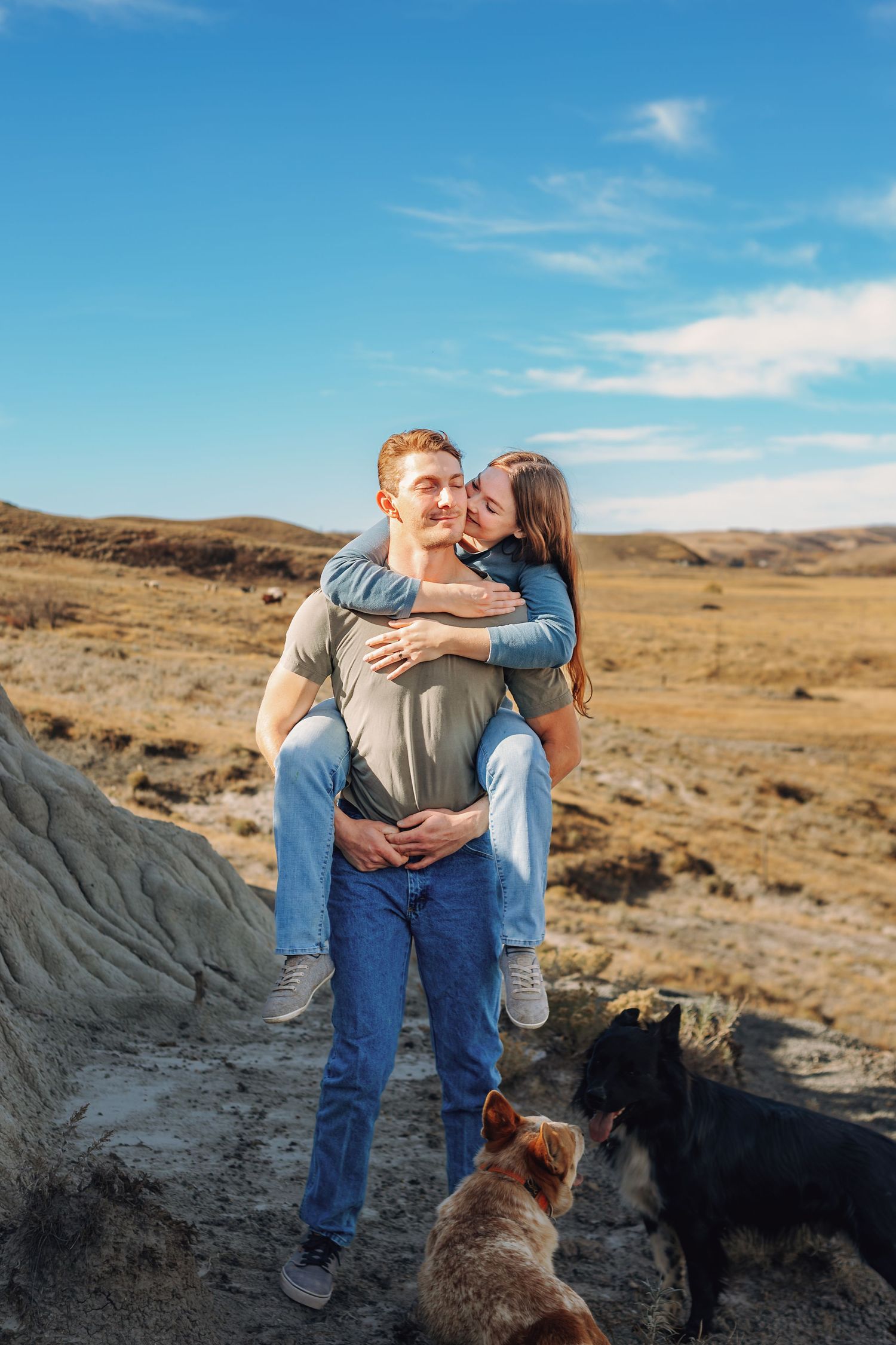 Couple sitting on rocky terrain with their dog against a blue sky backdrop.