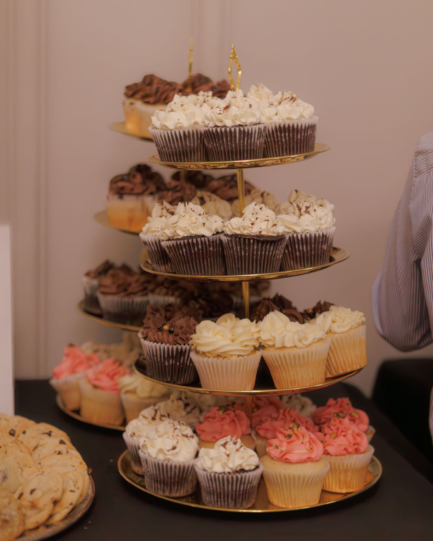 Tiered display of chocolate and vanilla cupcakes with white frosting on a dessert stand.