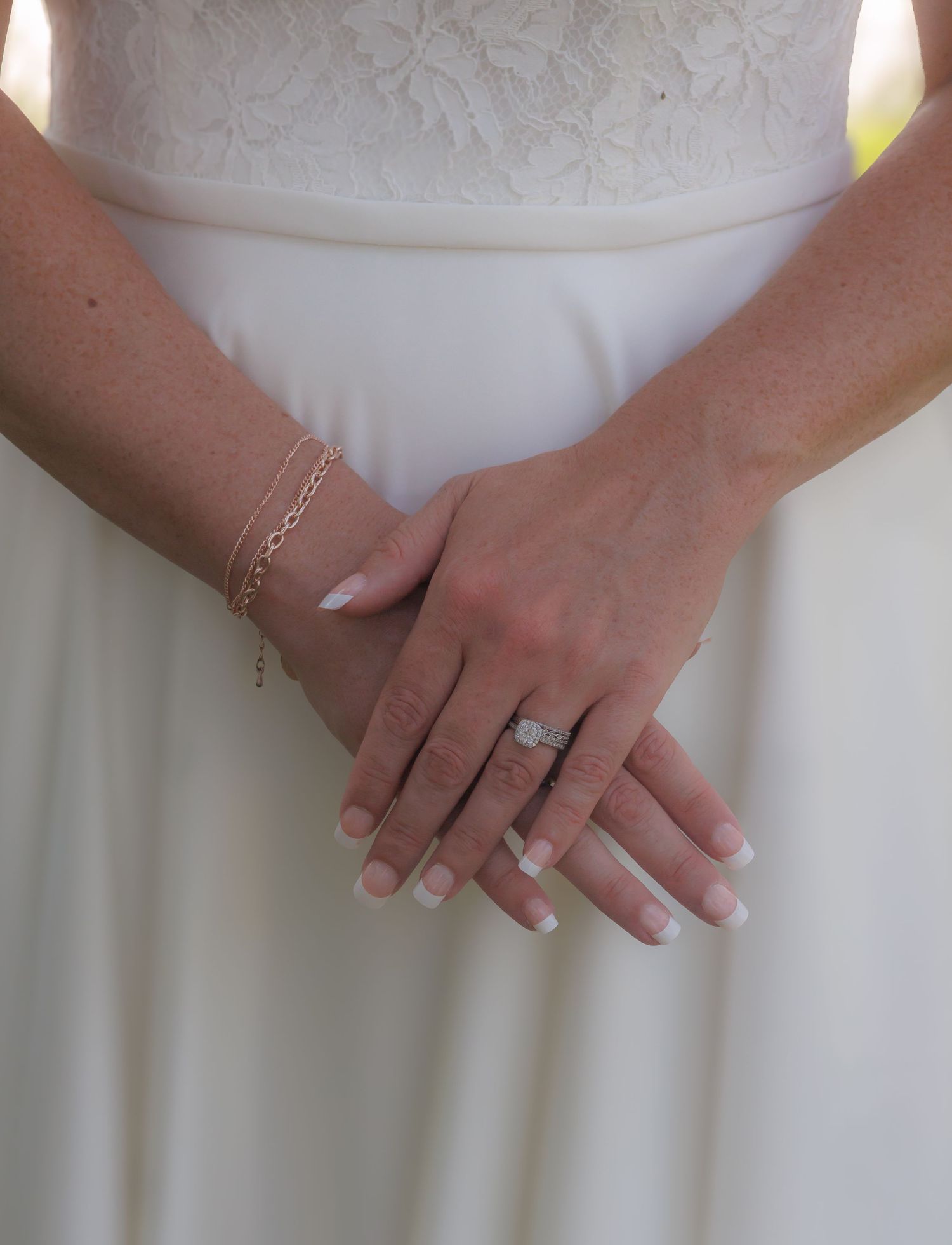 Close-up of hands in white dress showing wedding ring details.