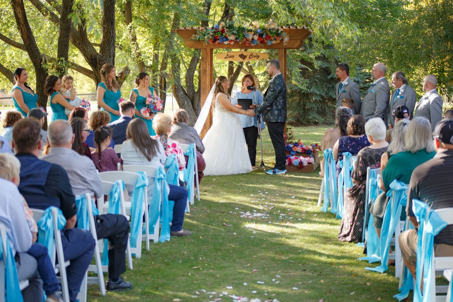 Outdoor wedding ceremony setup with turquoise chair decorations and natural backdrop.