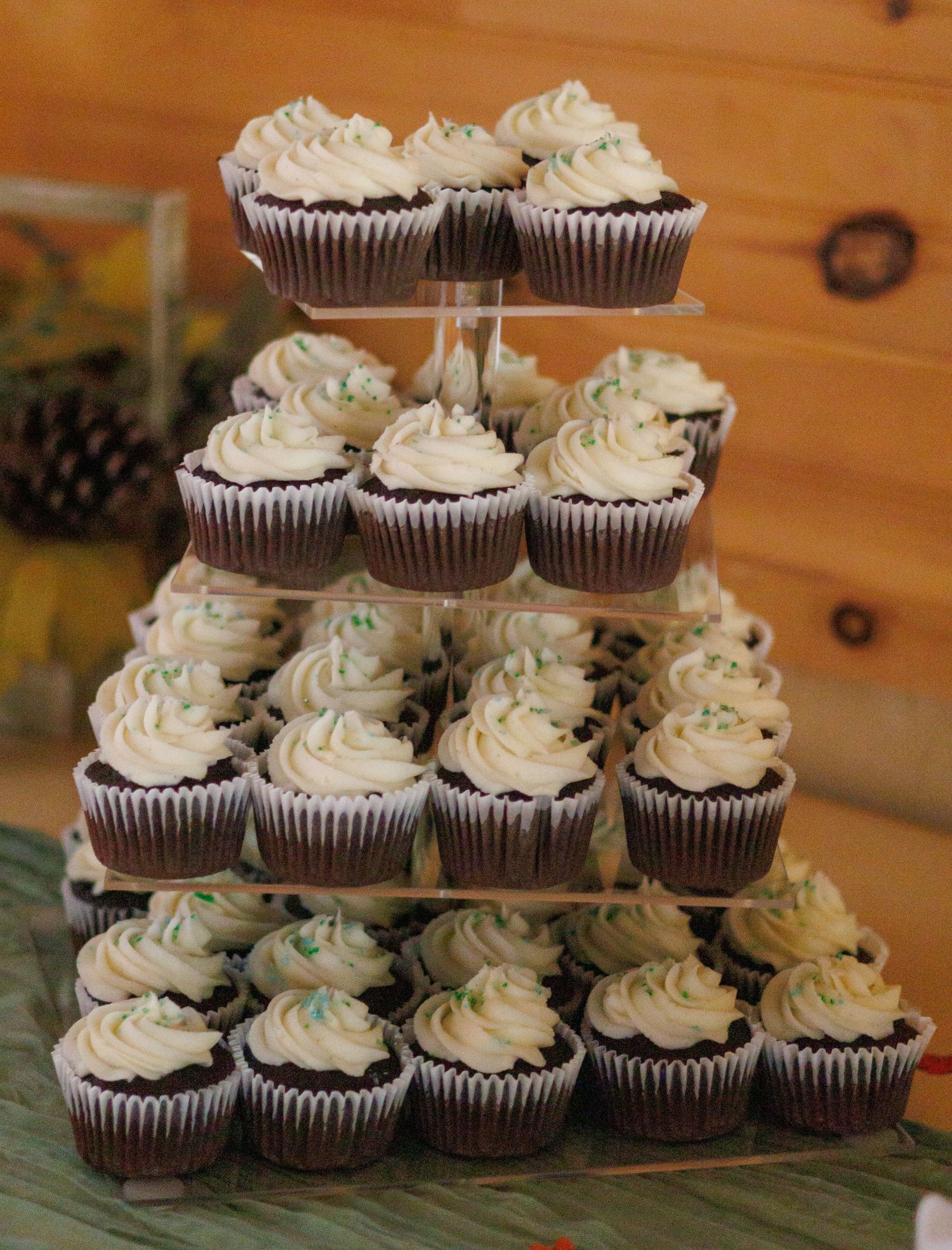 Chocolate cupcakes with white frosting and blue sprinkles arranged in tiers on display stands.