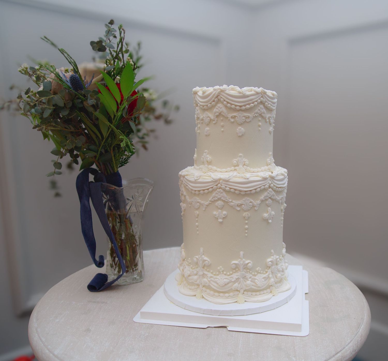 Elegant white wedding cake with delicate lace patterns and floral decorations displayed on a white stand.