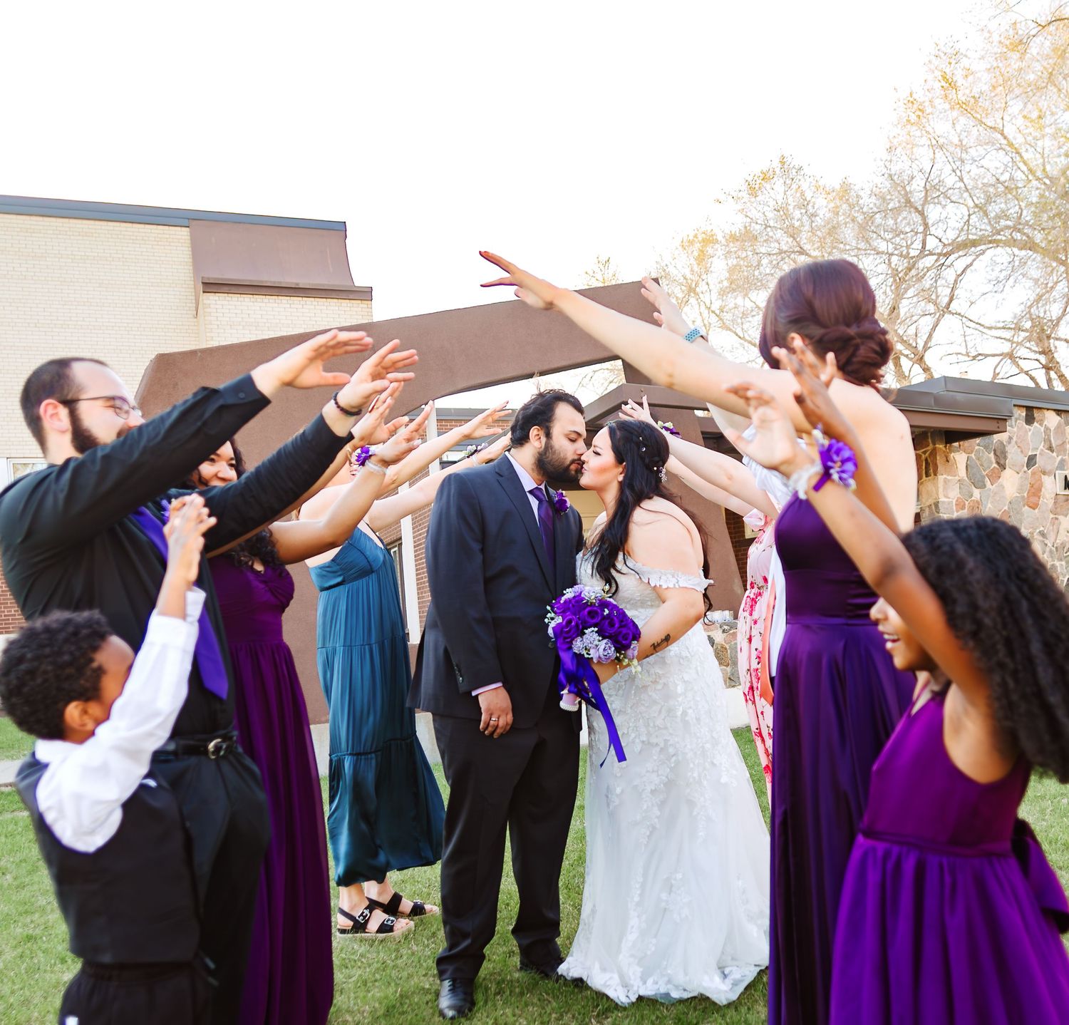 Wedding party performs synchronized dabbing pose outdoors in purple and black formal attire.