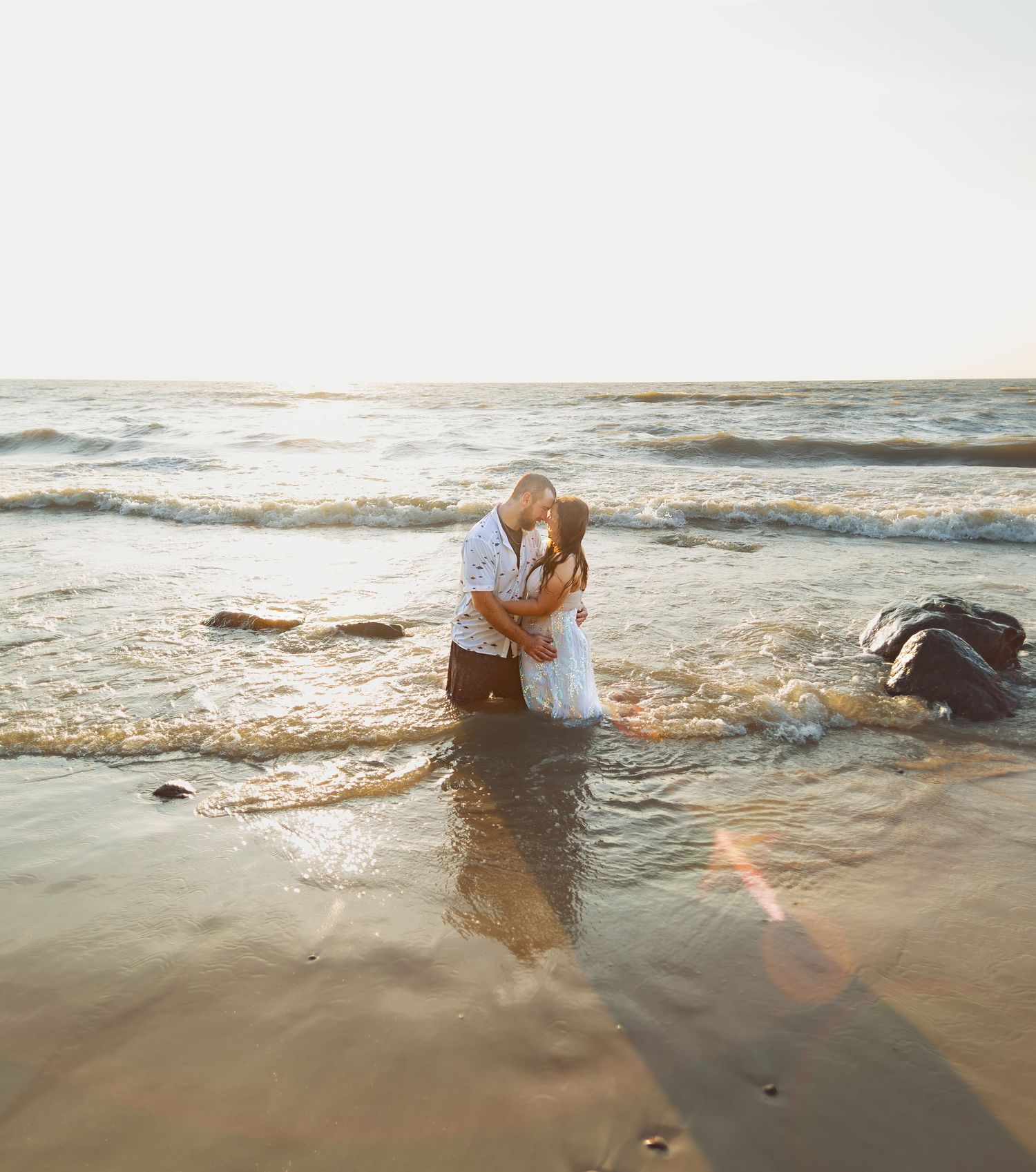 Artistic wedding photography session with water splashing on sandy beach at sunset.