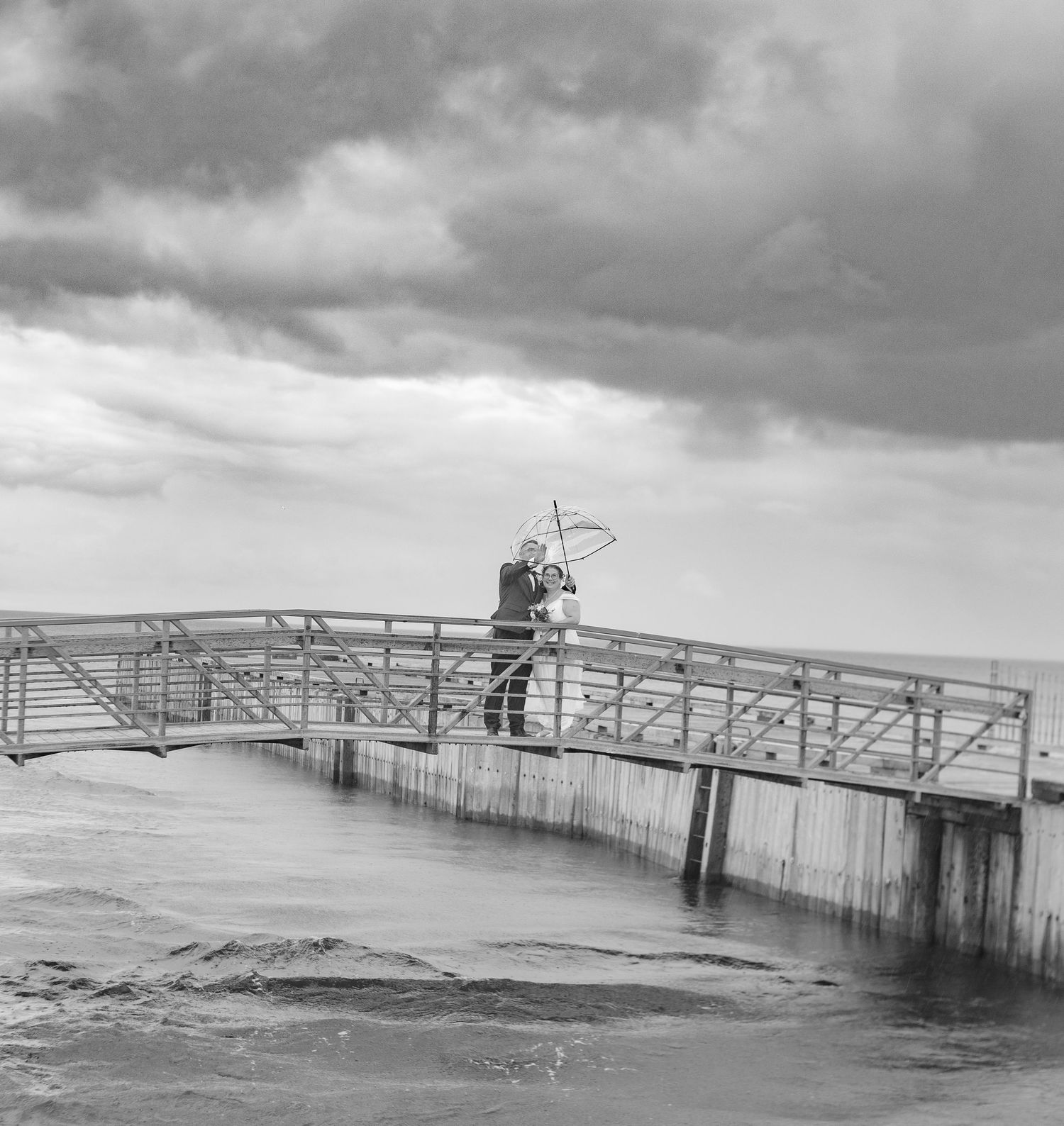 Black and white photograph of a dramatic wooden pier extending into rough waters.