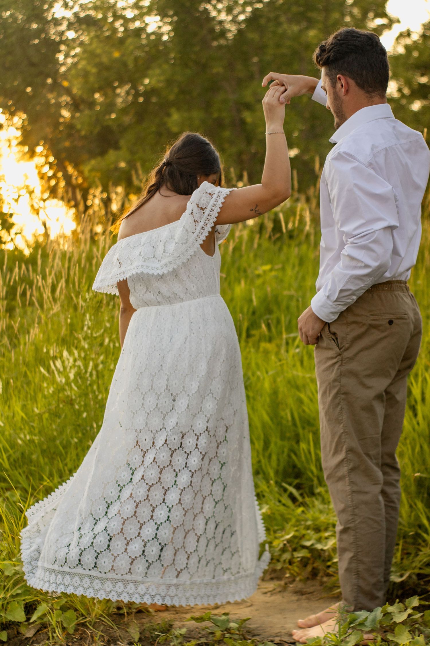 A couple dancing in a field, with the woman wearing a white lace dress and man in khaki pants.
