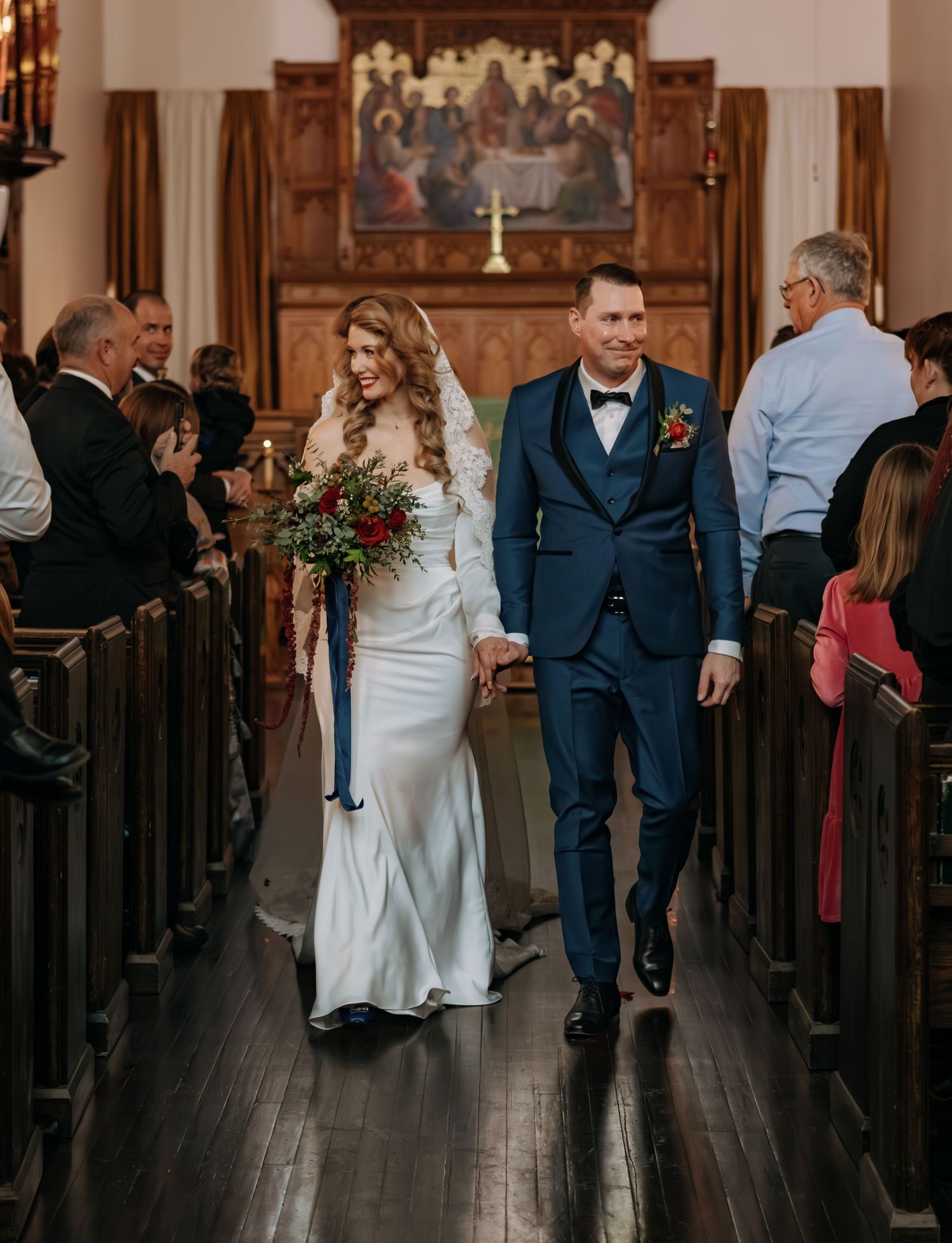 Wedding party processes down church aisle with wooden pews and decorative wall panels.