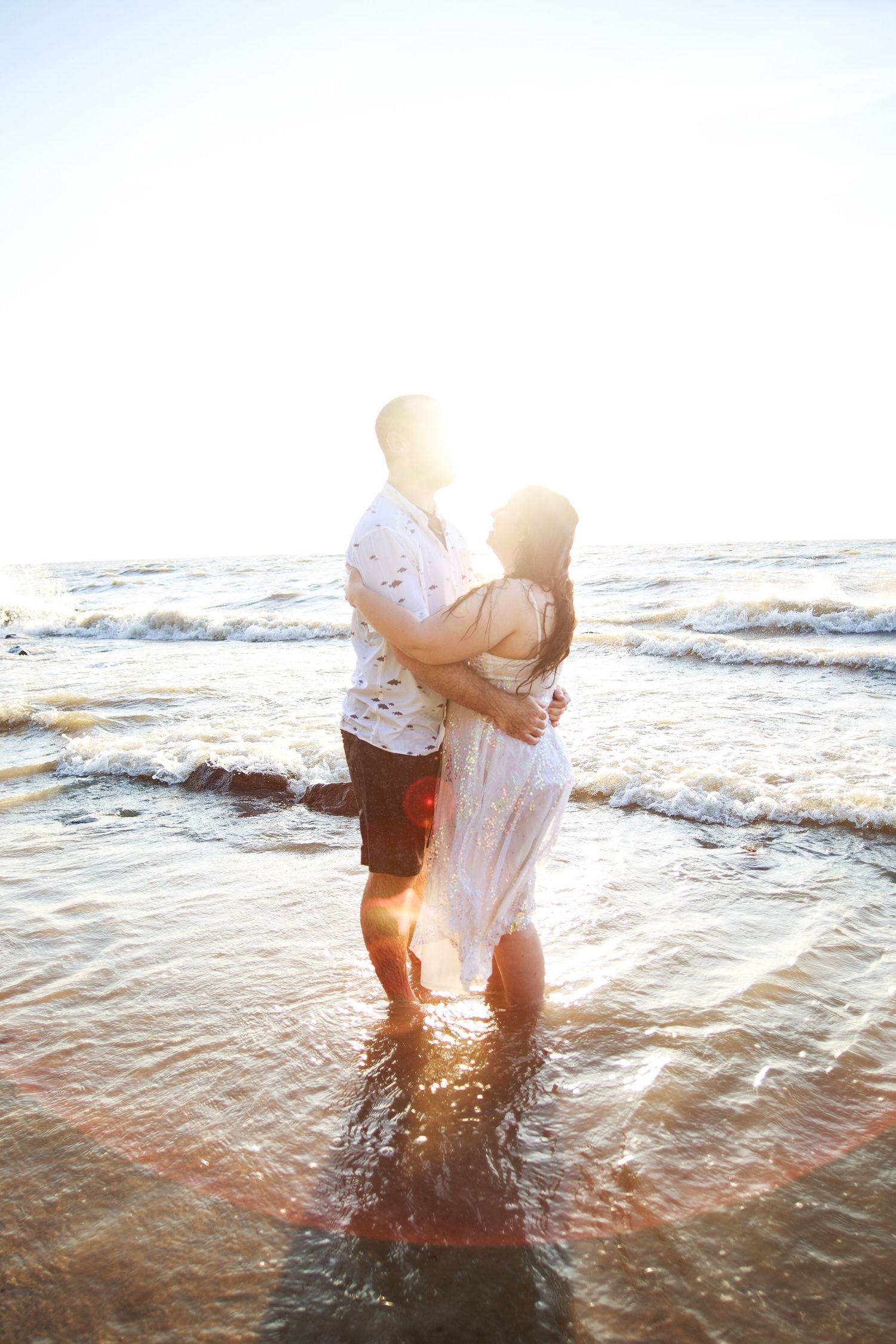 A romantic sunset embrace in shallow ocean waters with waves rolling in.
