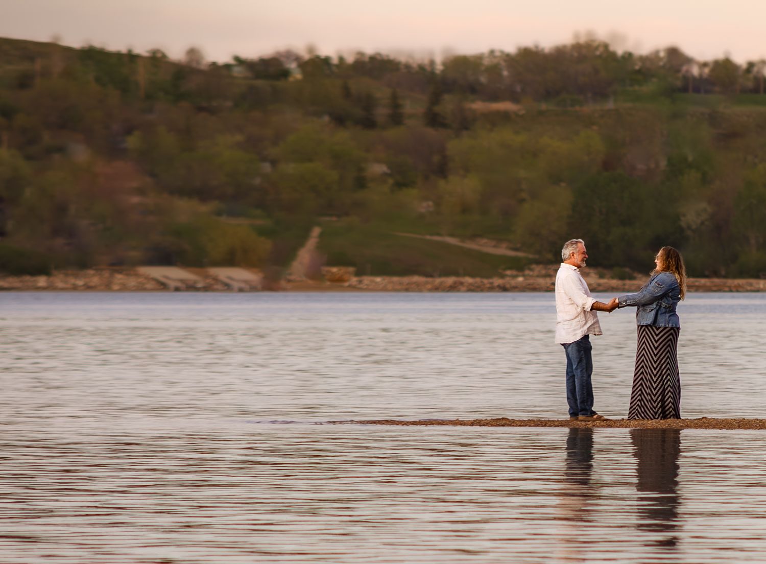 Romantic couple embracing by a large tree trunk at sunset near a lake.