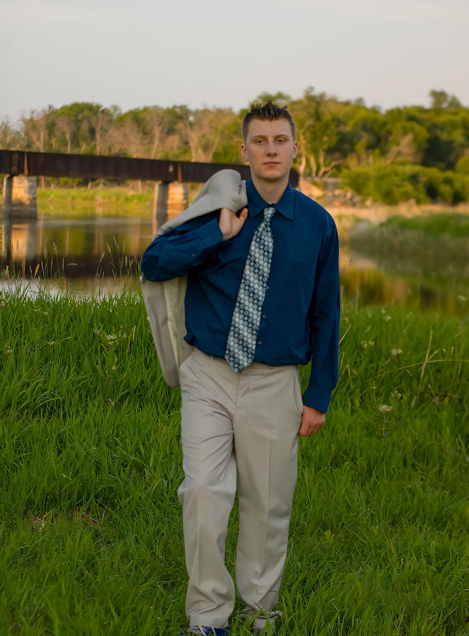 Outdoor portrait session in formal wear against lush green field and water backdrop.