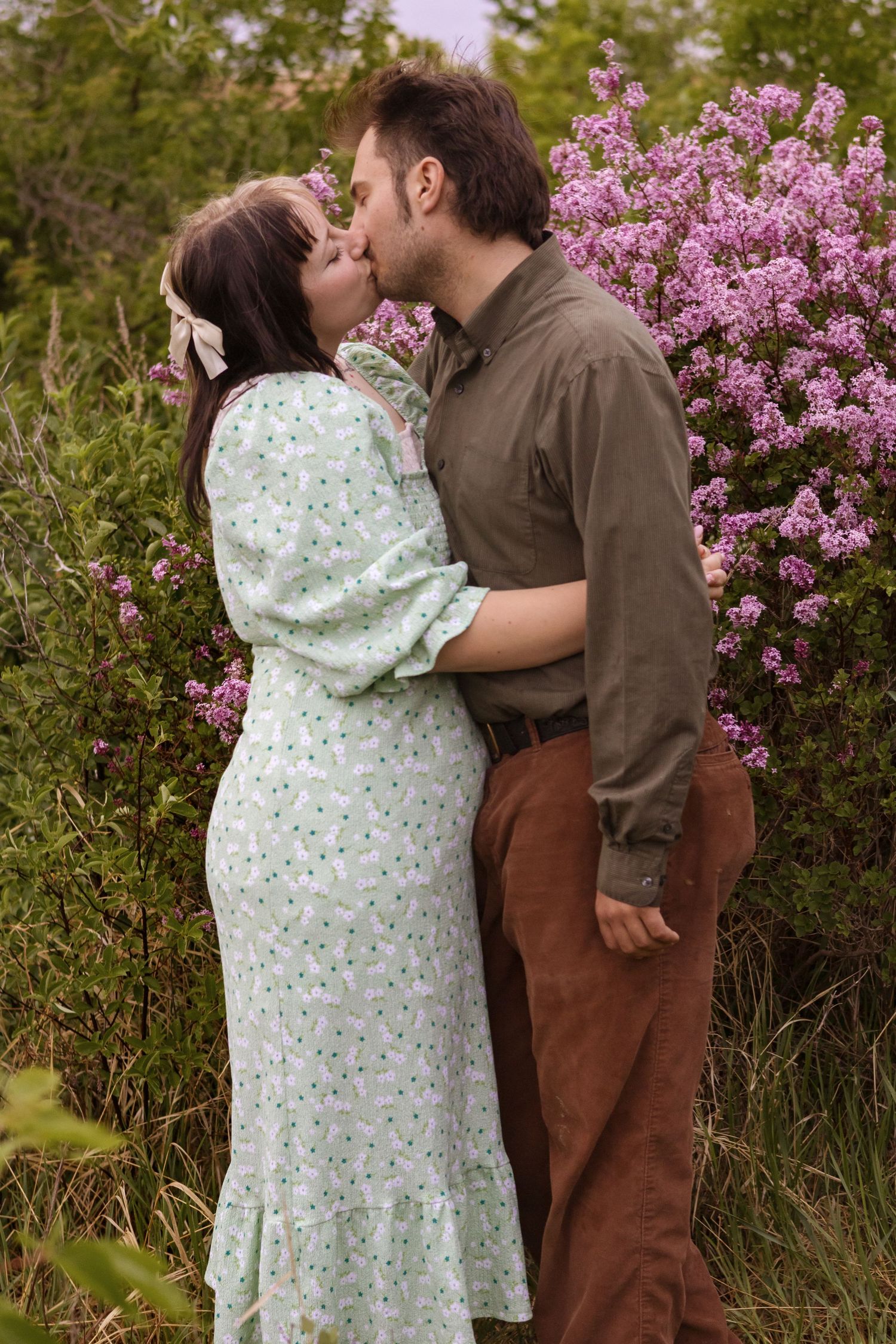 A romantic couple embraces near blooming lilac bushes in springtime.