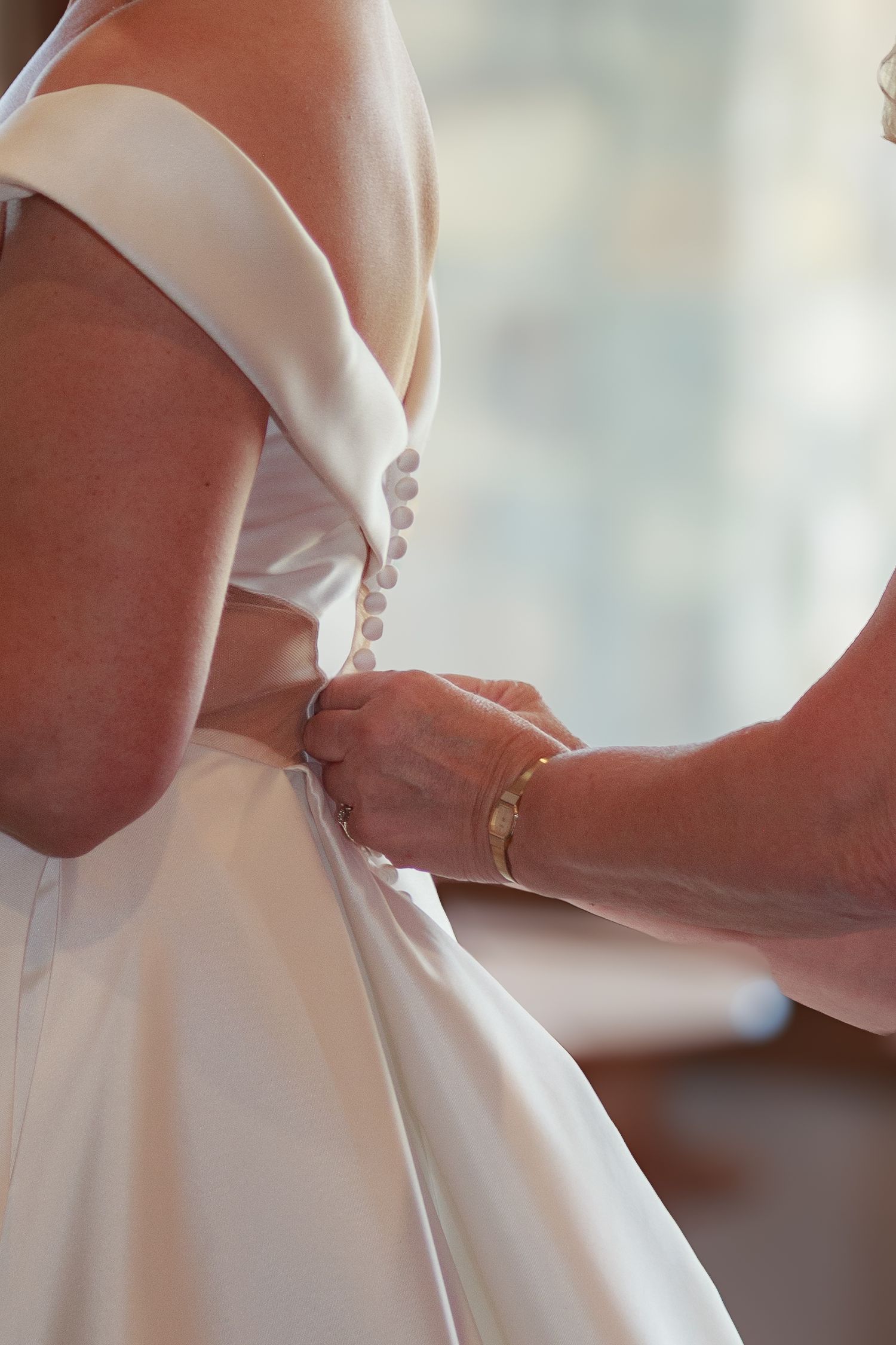 Detail shot of elegant white wedding dress being adjusted with careful precision.