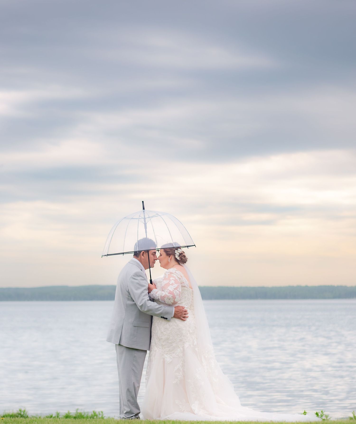 A romantic rainy day wedding photo with couple sharing umbrella by waterfront.