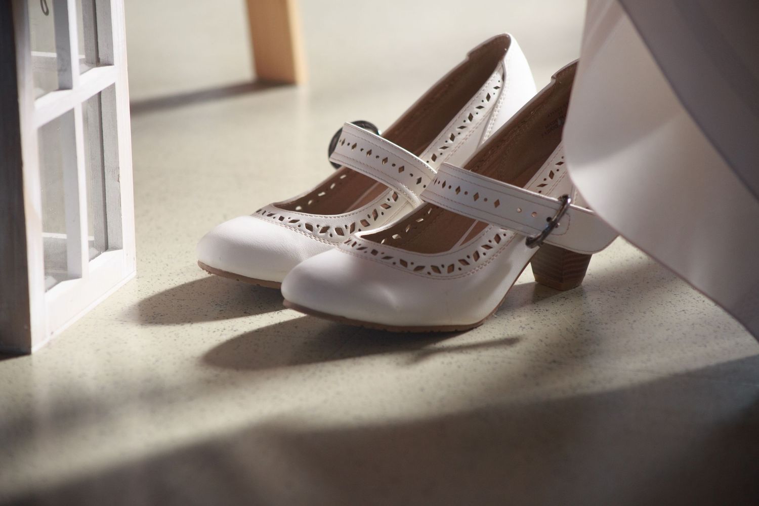 Elegant bridal shoes placed near a window with natural lighting casting shadows.