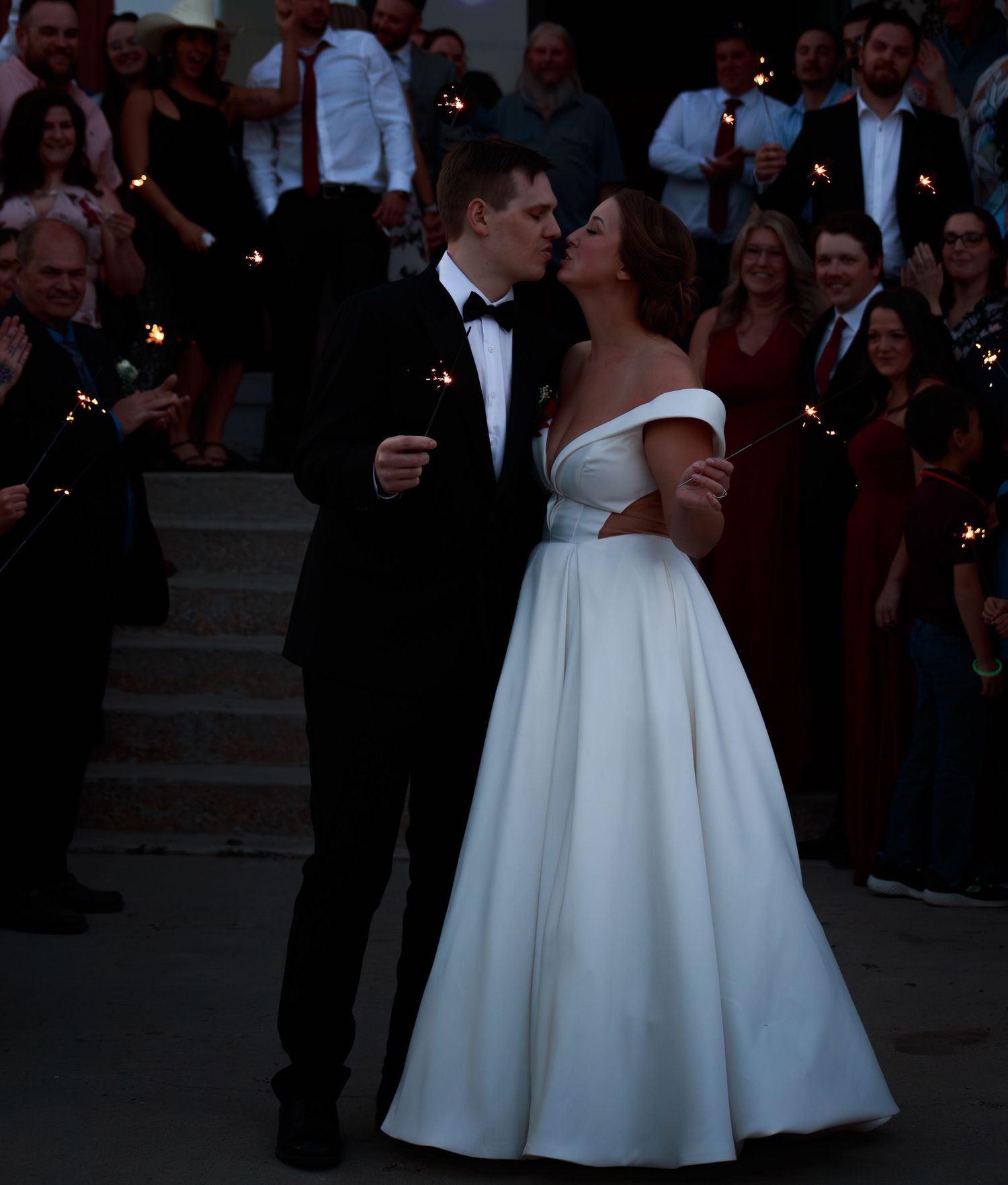 Wedding party in formal attire standing on steps at an evening celebration.