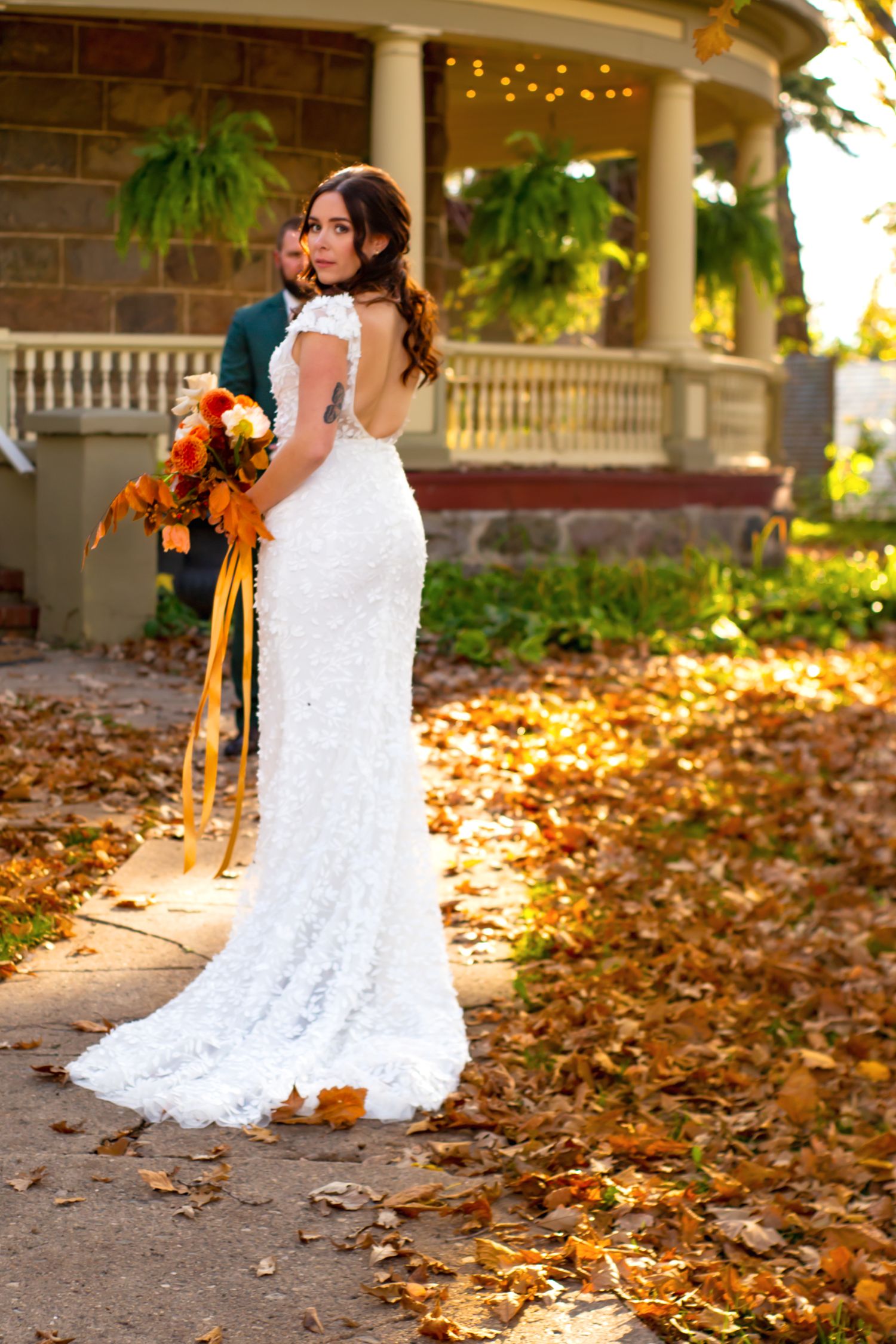 Autumn wedding scene with fallen leaves on ground near white pillars and string lights.