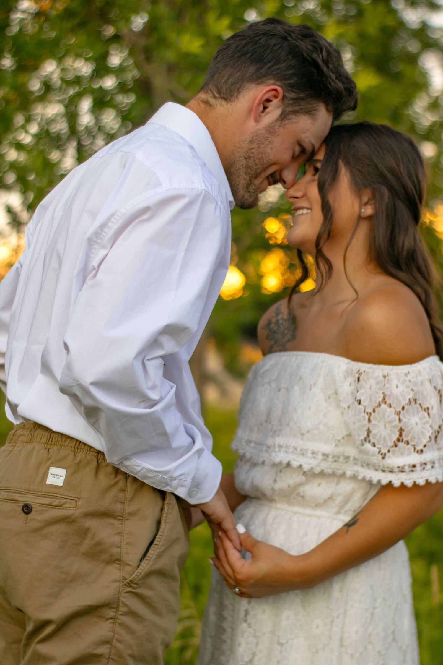 A couple in white and khaki outfits sharing a romantic moment in a grassy field at sunset.