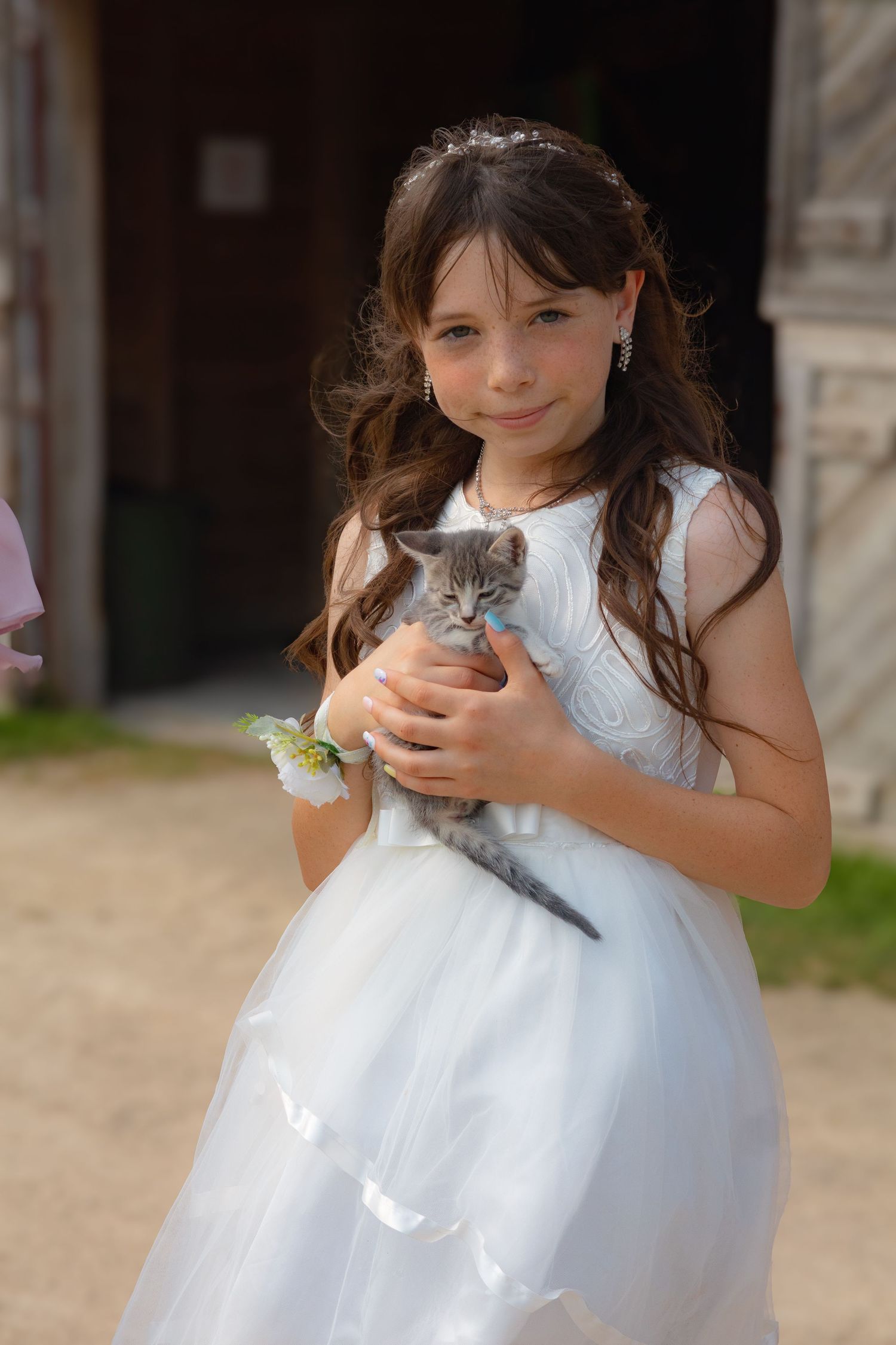 A flower girl in a white dress holds a small furry animal during a wedding celebration.