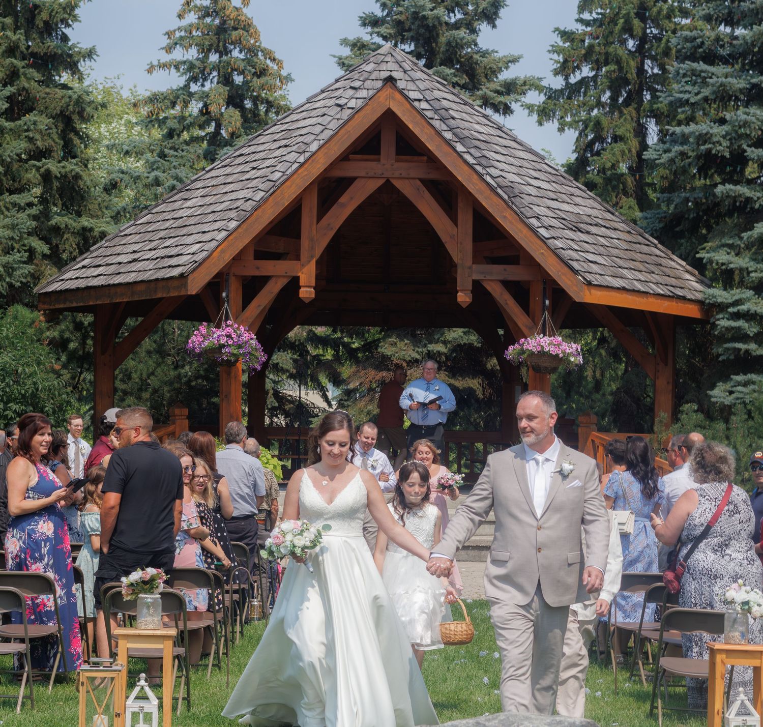 Wedding ceremony taking place under a rustic wooden pavilion surrounded by tall pine trees.