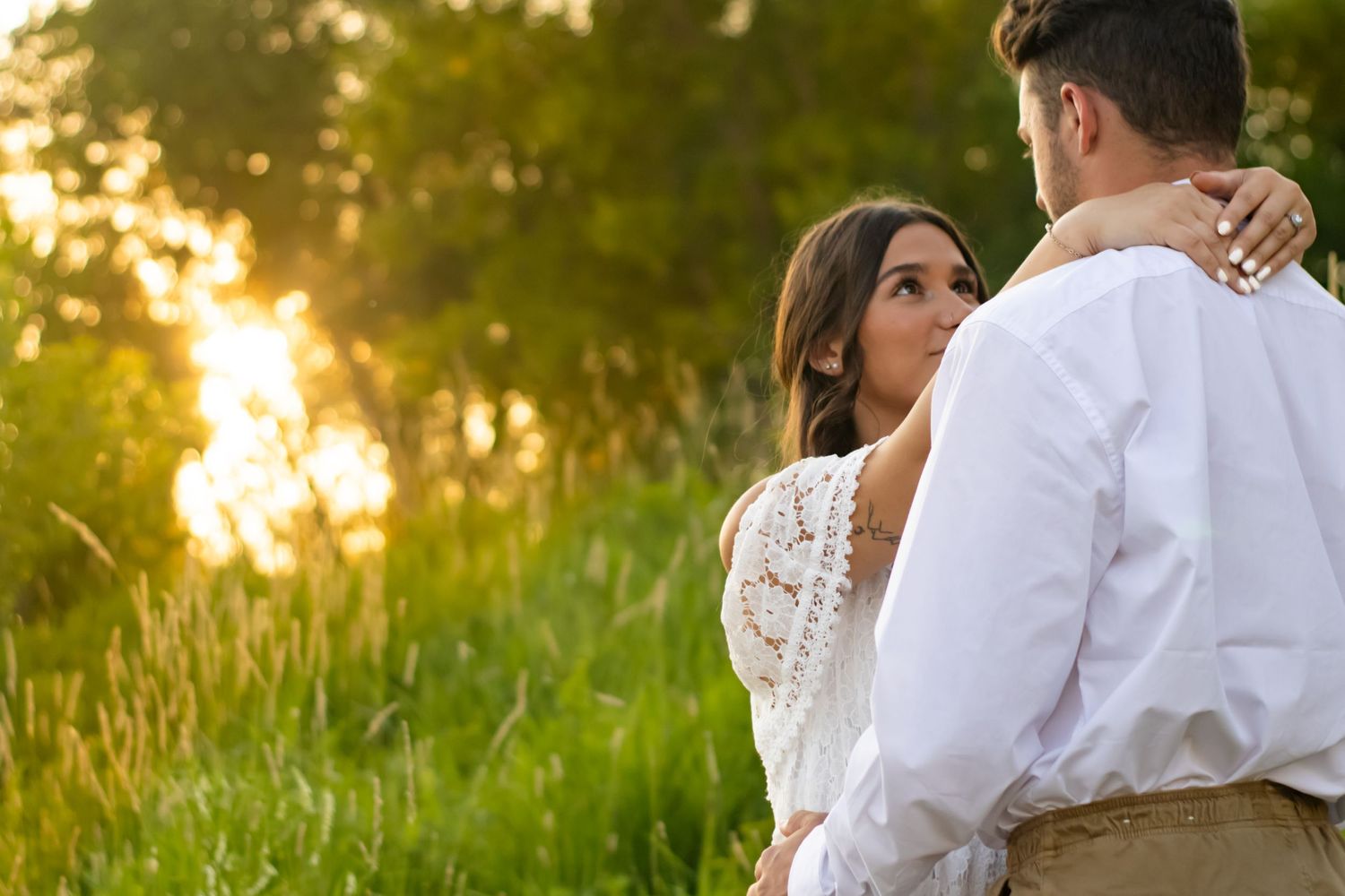 A couple in white clothing embracing in a sunlit meadow during golden hour.