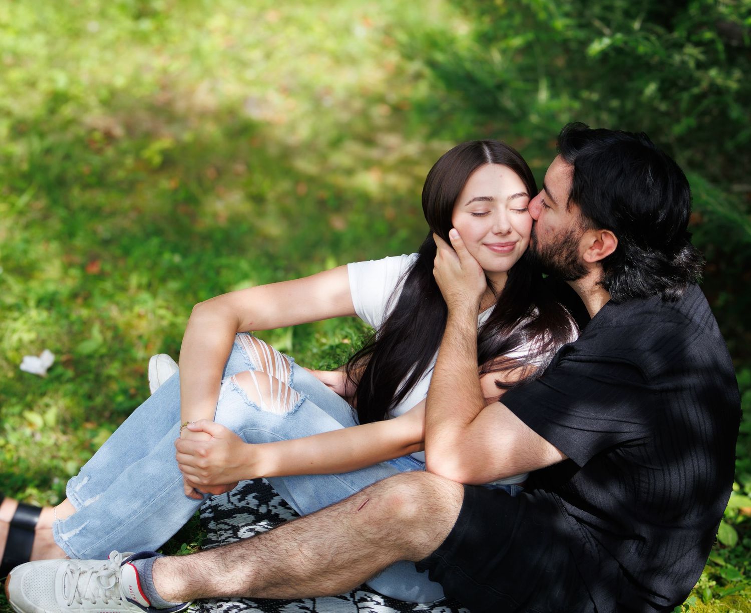 A couple shares an intimate moment while lying in green grass outdoors.
