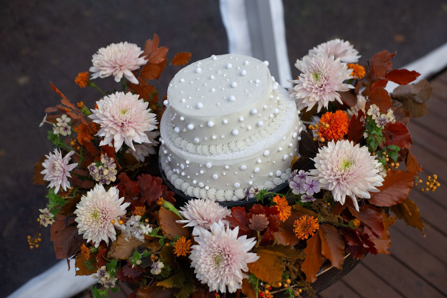 Wedding cake decorated with pink dahlias and orange flowers on a dark wooden surface.