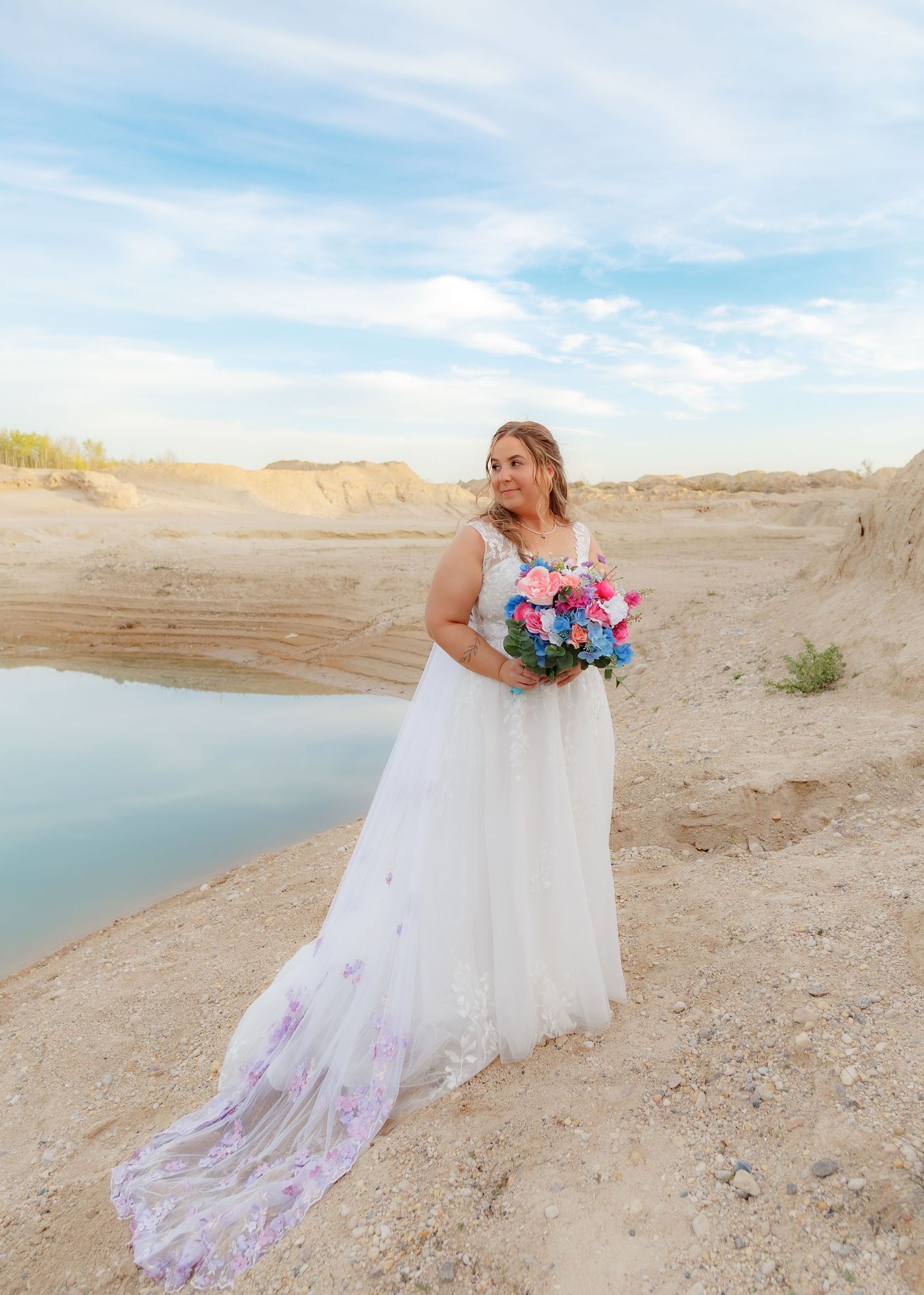 Bridal portraits on sandy shoreline with flowing white dress and colorful bouquet.