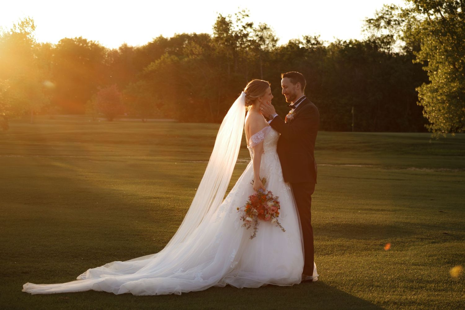Silhouetted wedding couple walking across a field at sunset.