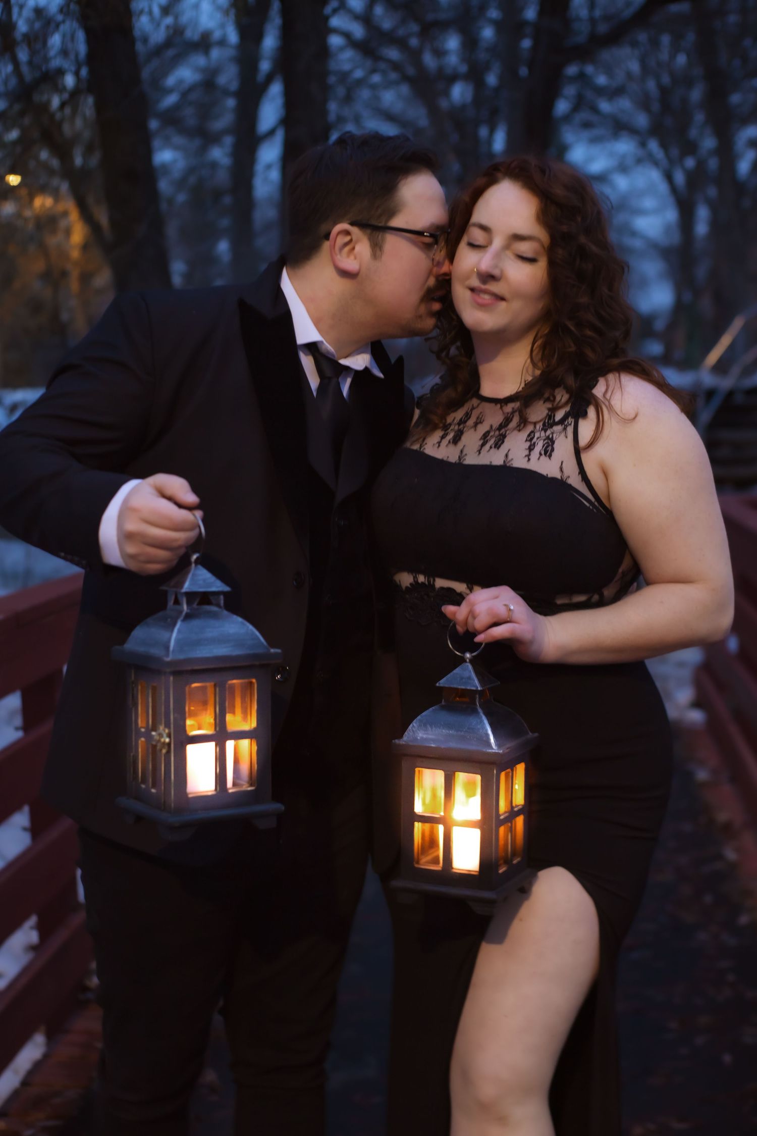 Romantic couple posing with glowing lanterns at twilight in winter setting.