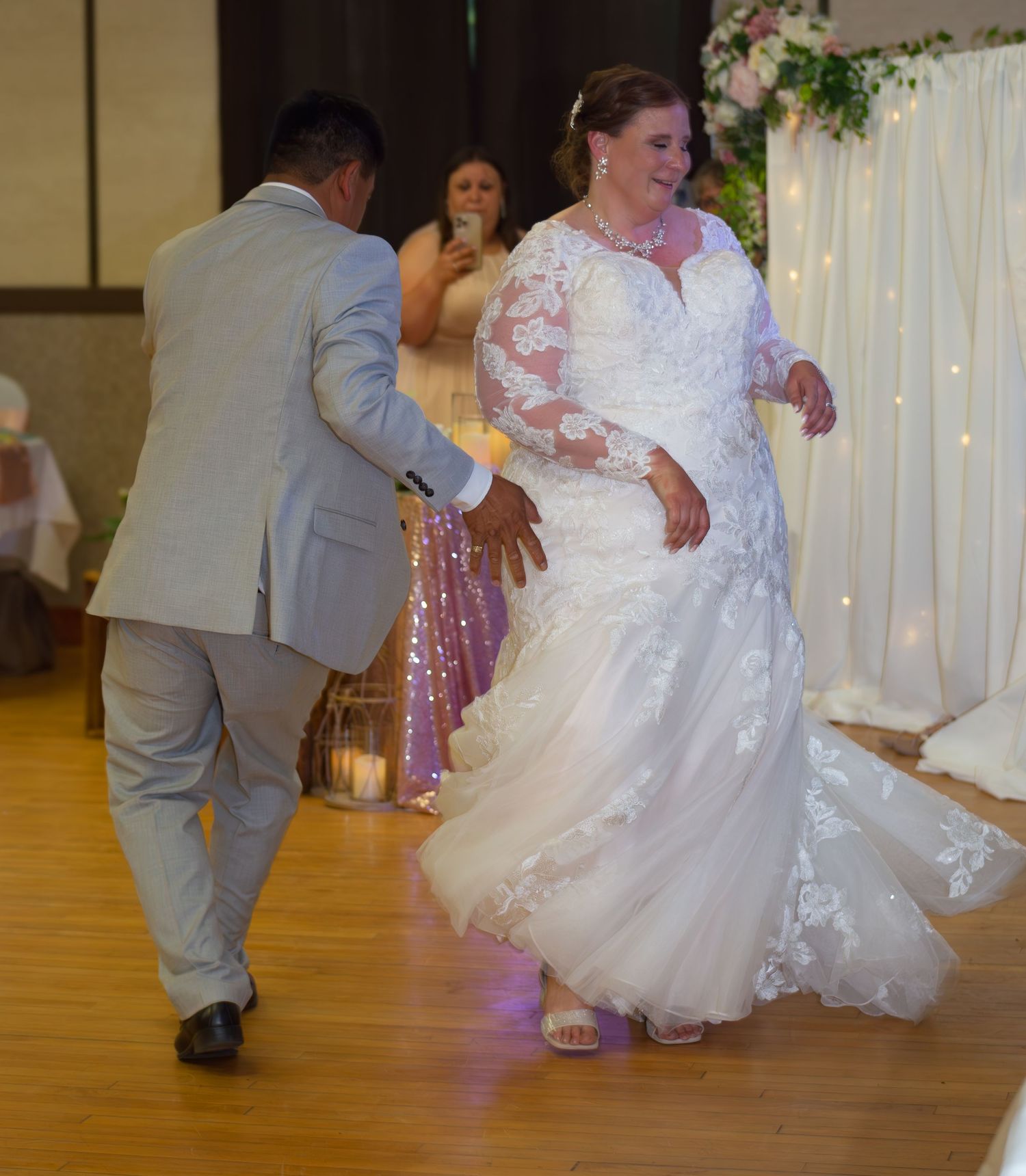 Wedding reception dancing captured in motion on a wooden dance floor with decorative lights.