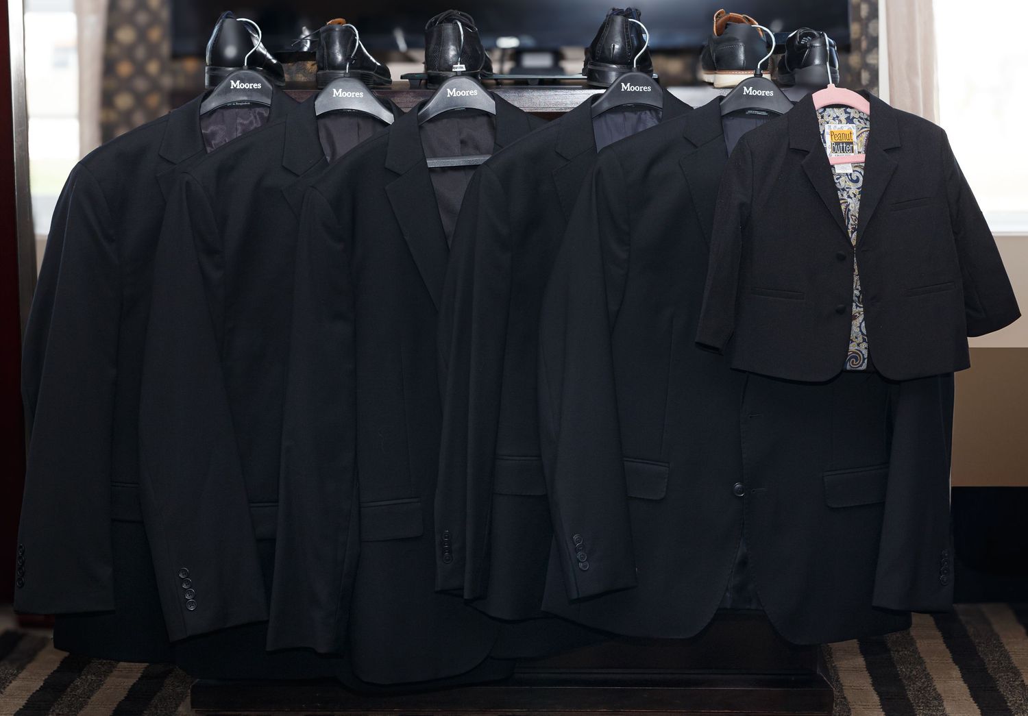Row of black suits hanging neatly on hangers against dark background.