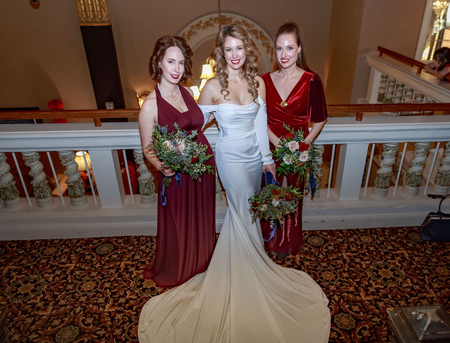 Bridesmaids in burgundy dresses posing together in an elegant venue hallway.