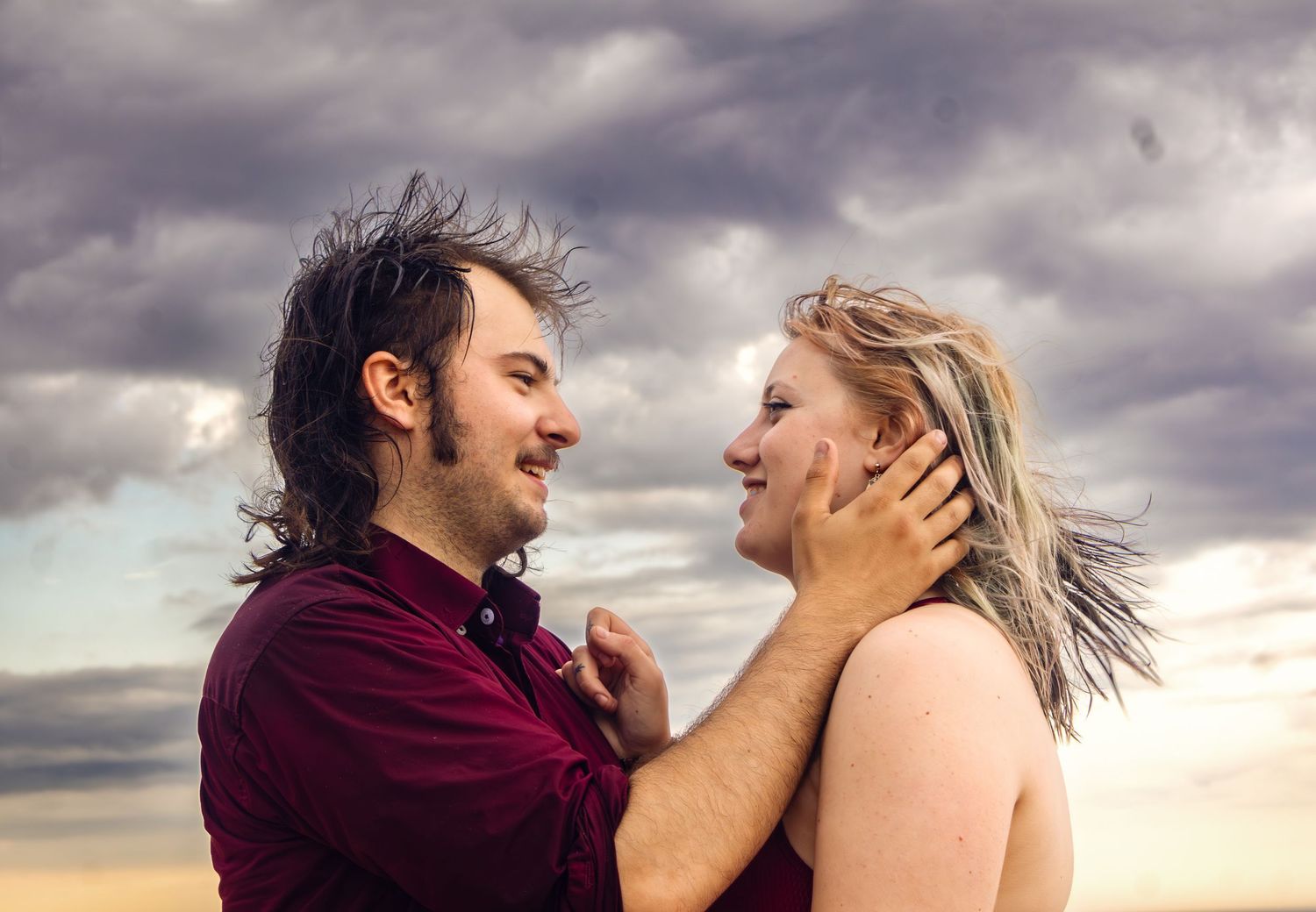 A couple sharing an emotional moment against a dramatic cloudy beach sunset.